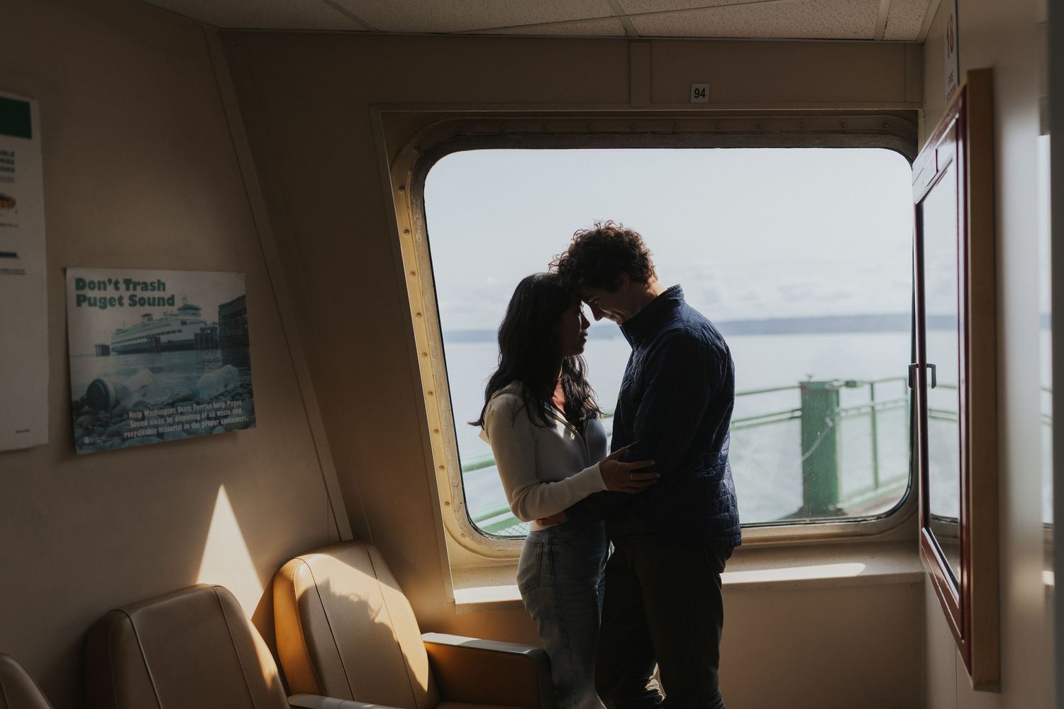 Couple sharing an intimate moment by a window on a ferry boat, backlit by natural light.