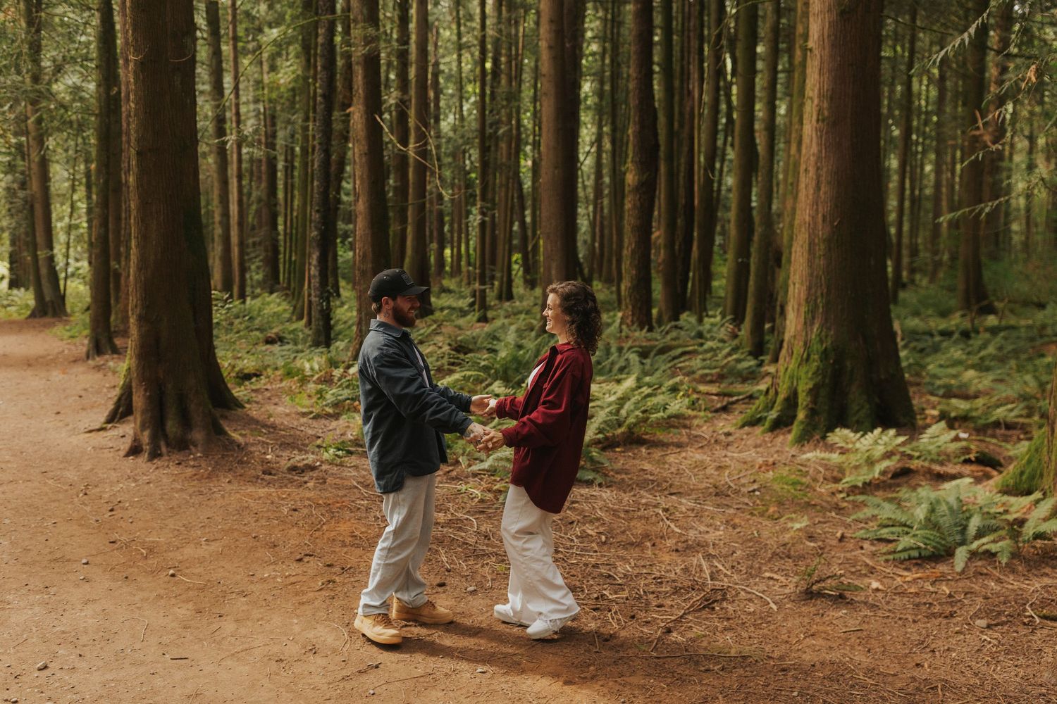 A couple shares a romantic dance moment on a sunlit forest trail.