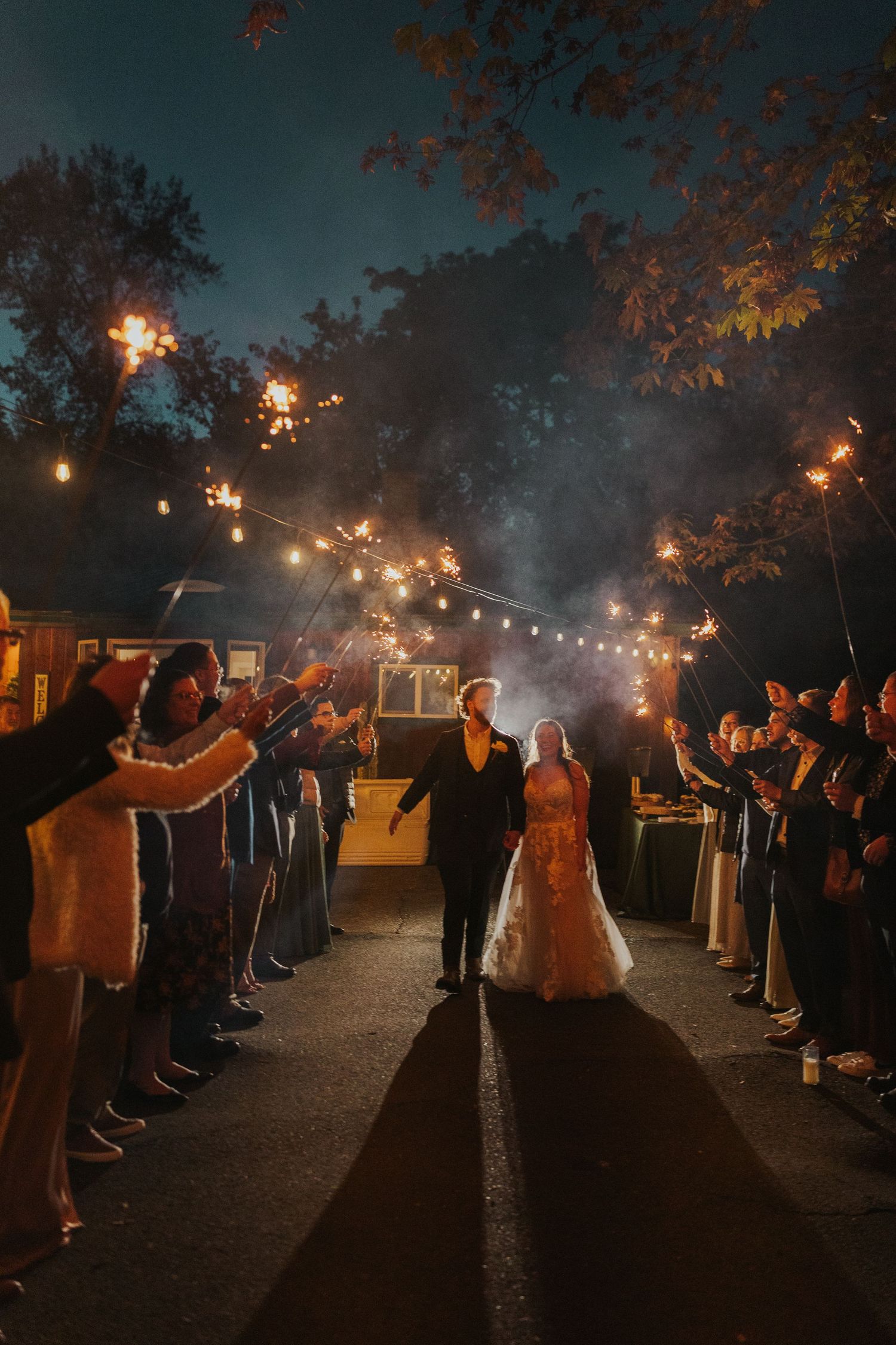 Nighttime wedding exit under string lights with sparkler sendoff from guests.