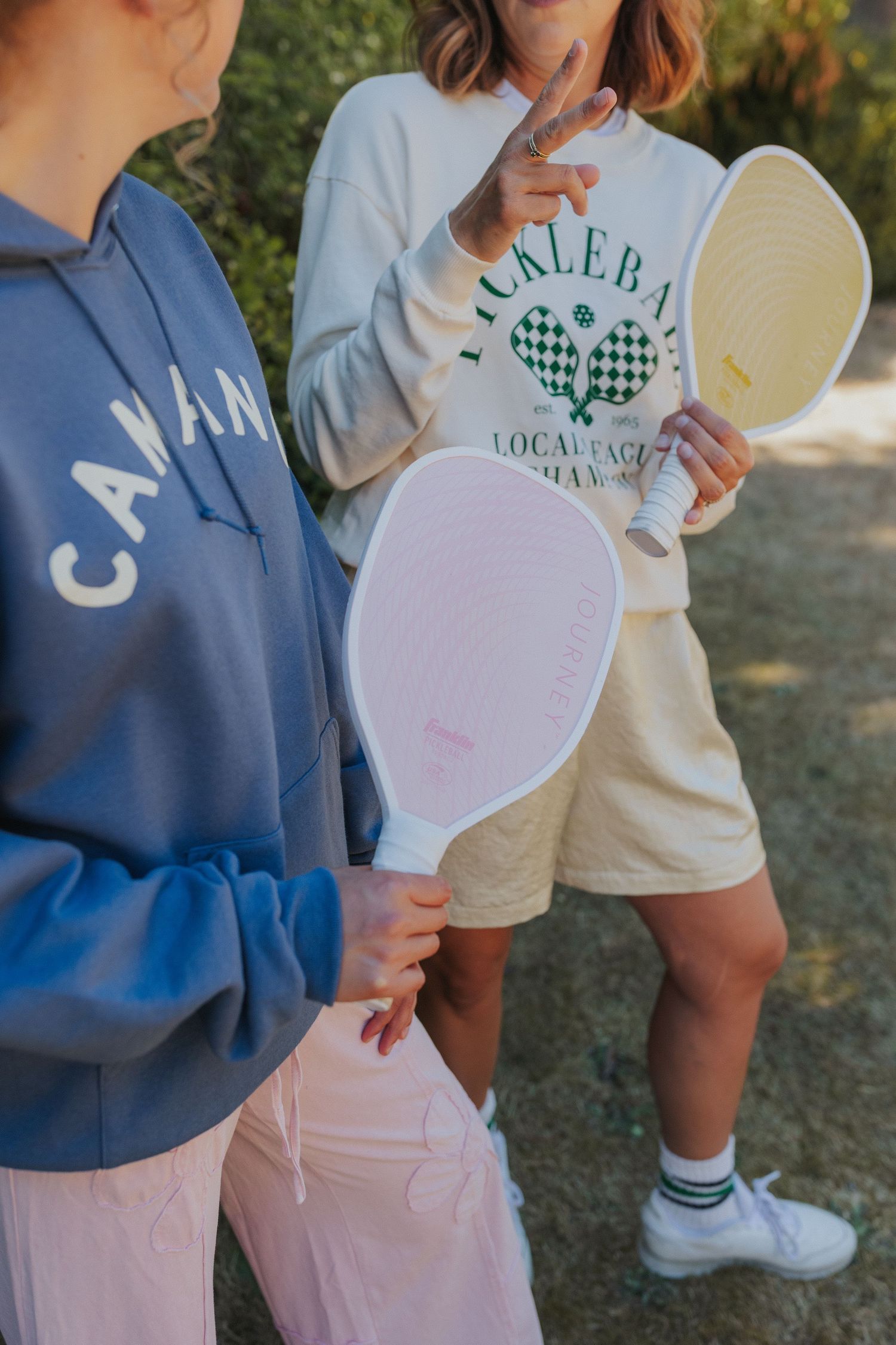 Two people in casual wear holding heart-shaped paper cutouts in an outdoor setting.