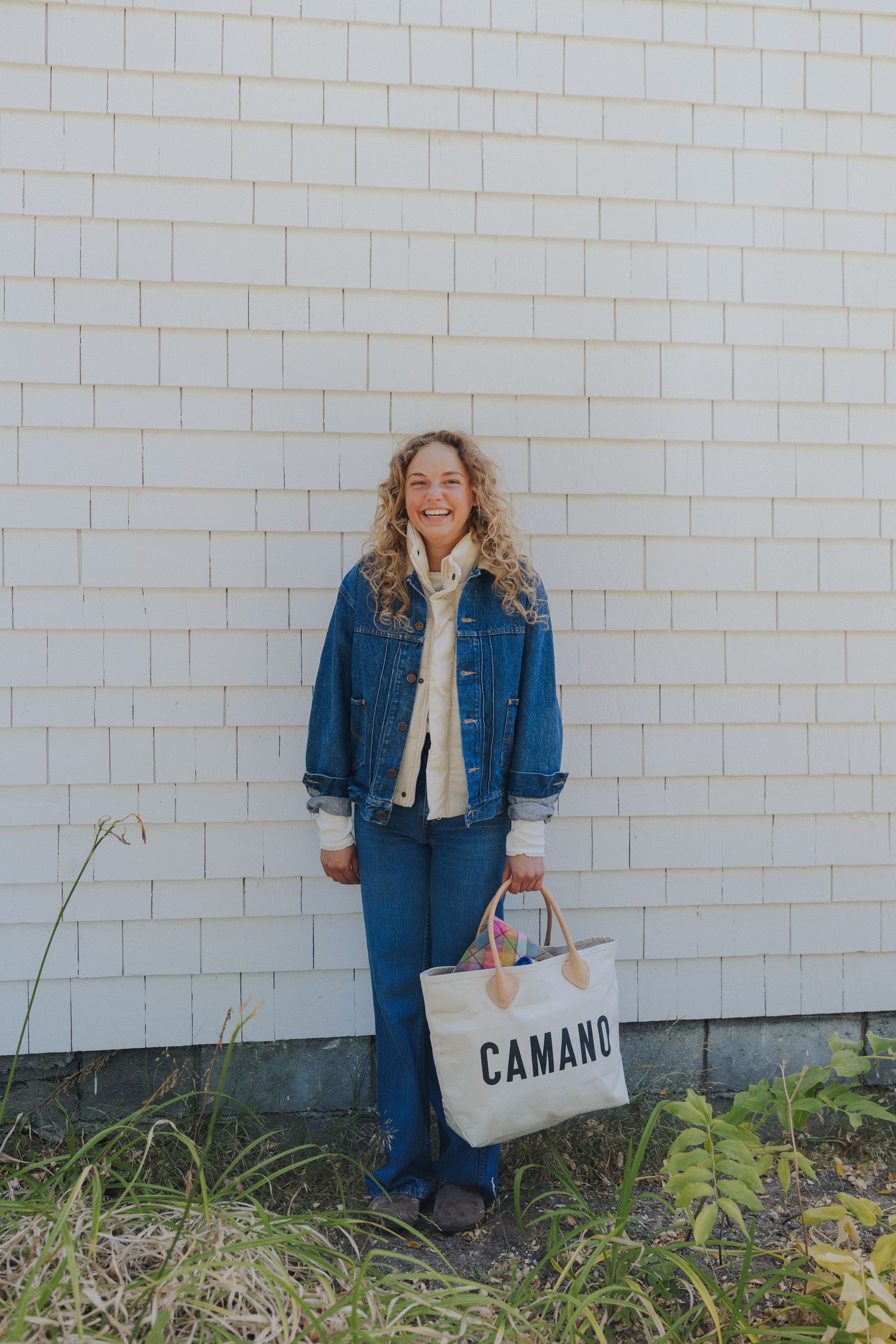 A casual fashion shoot against a white brick wall featuring denim and a canvas tote.