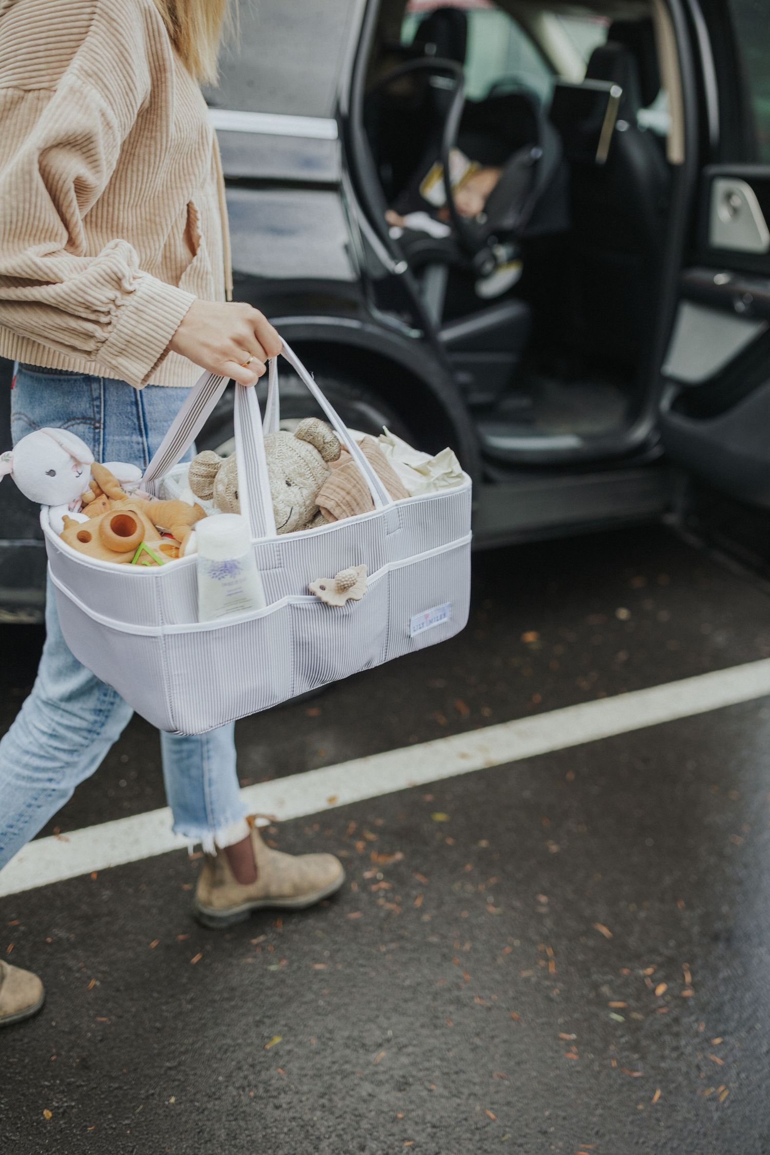 Someone carrying a white storage basket filled with toys through a parking lot.