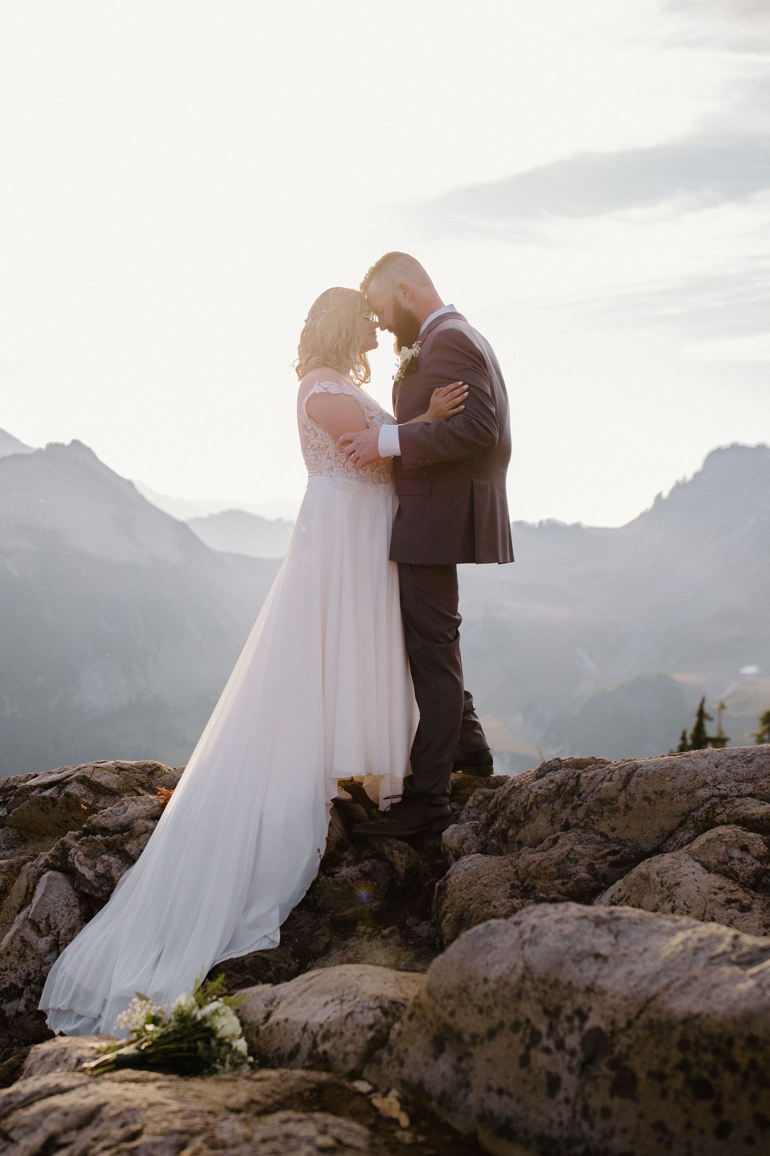 A romantic wedding moment captured in silhouette against misty mountain peaks at dusk.