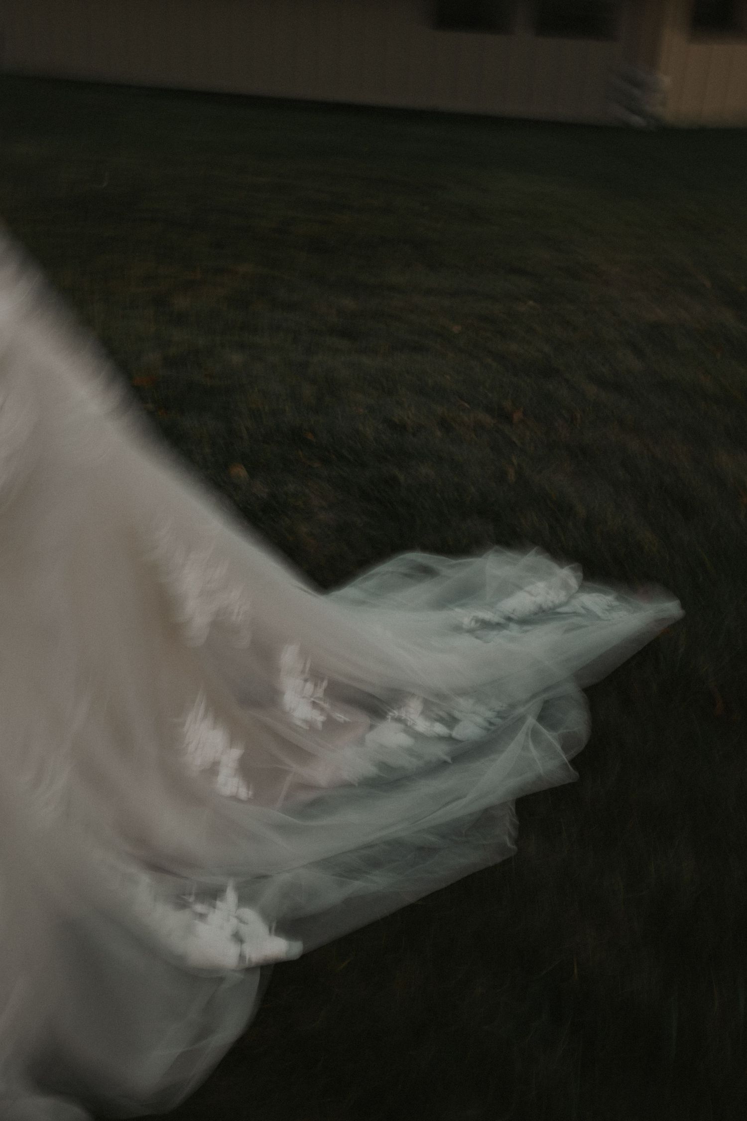 Flowing white wedding dress train creates an ethereal effect against a dark background.