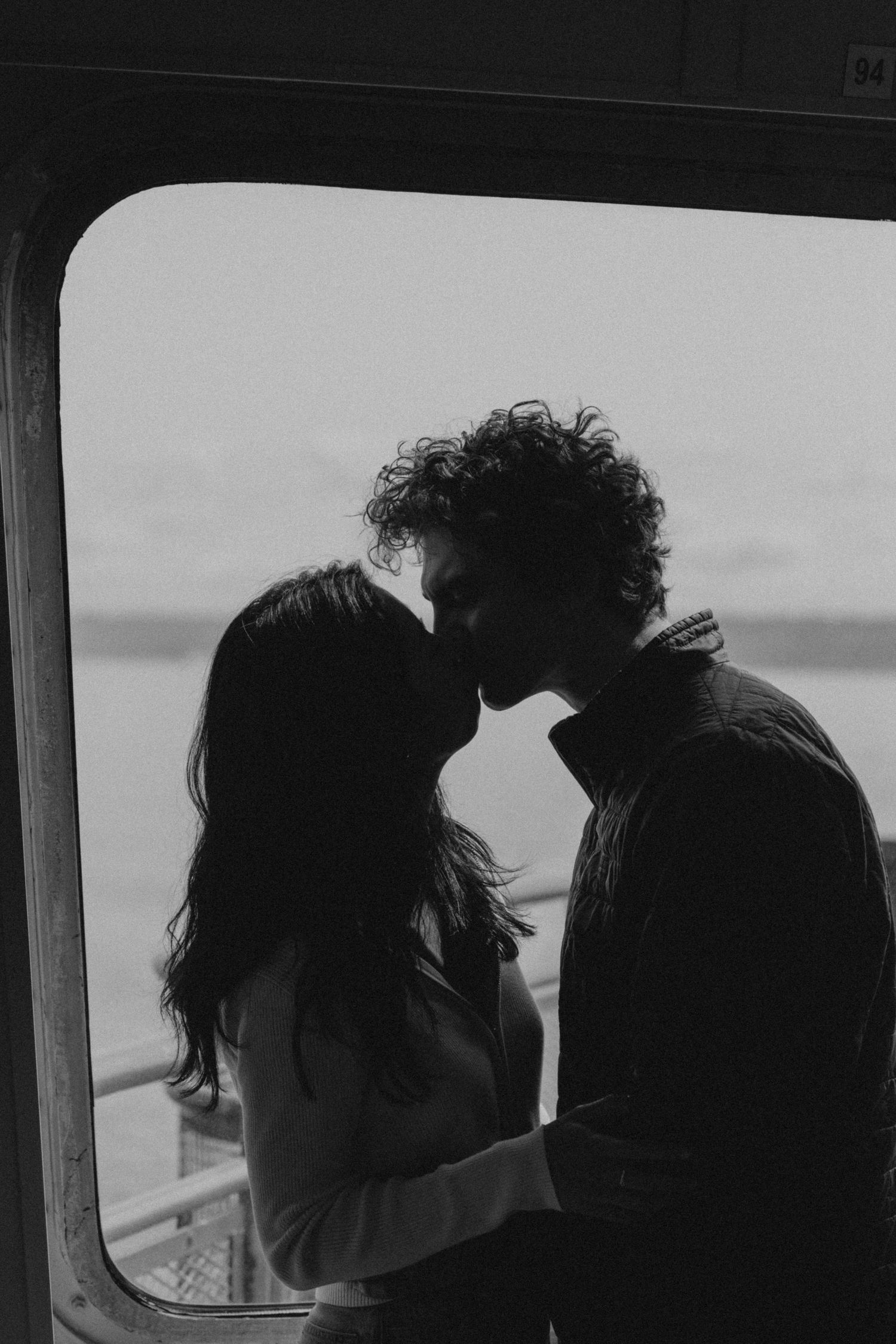 Dark silhouettes of two people in close conversation against bright window background.