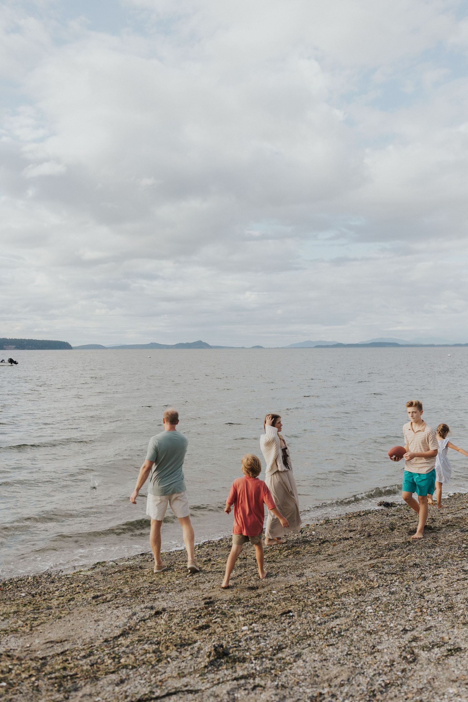 Group walking along a rocky beach shoreline on a cloudy day.