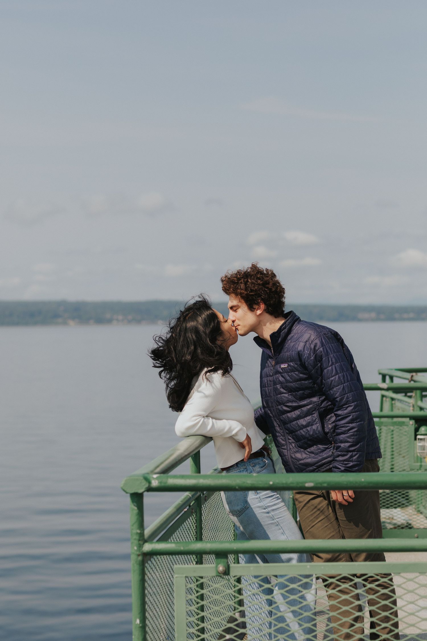 Two people share an intimate moment on a waterfront observation platform with serene ocean views.