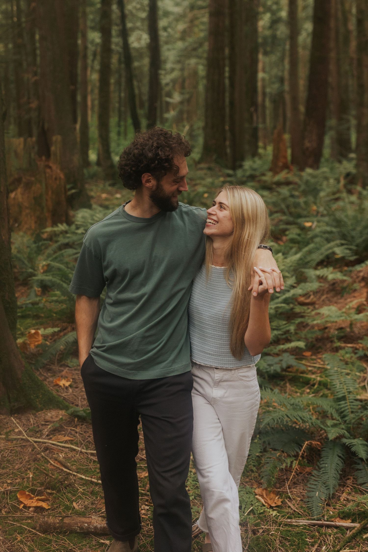 A couple shares a joyful moment together while walking through a lush forest with ferns.