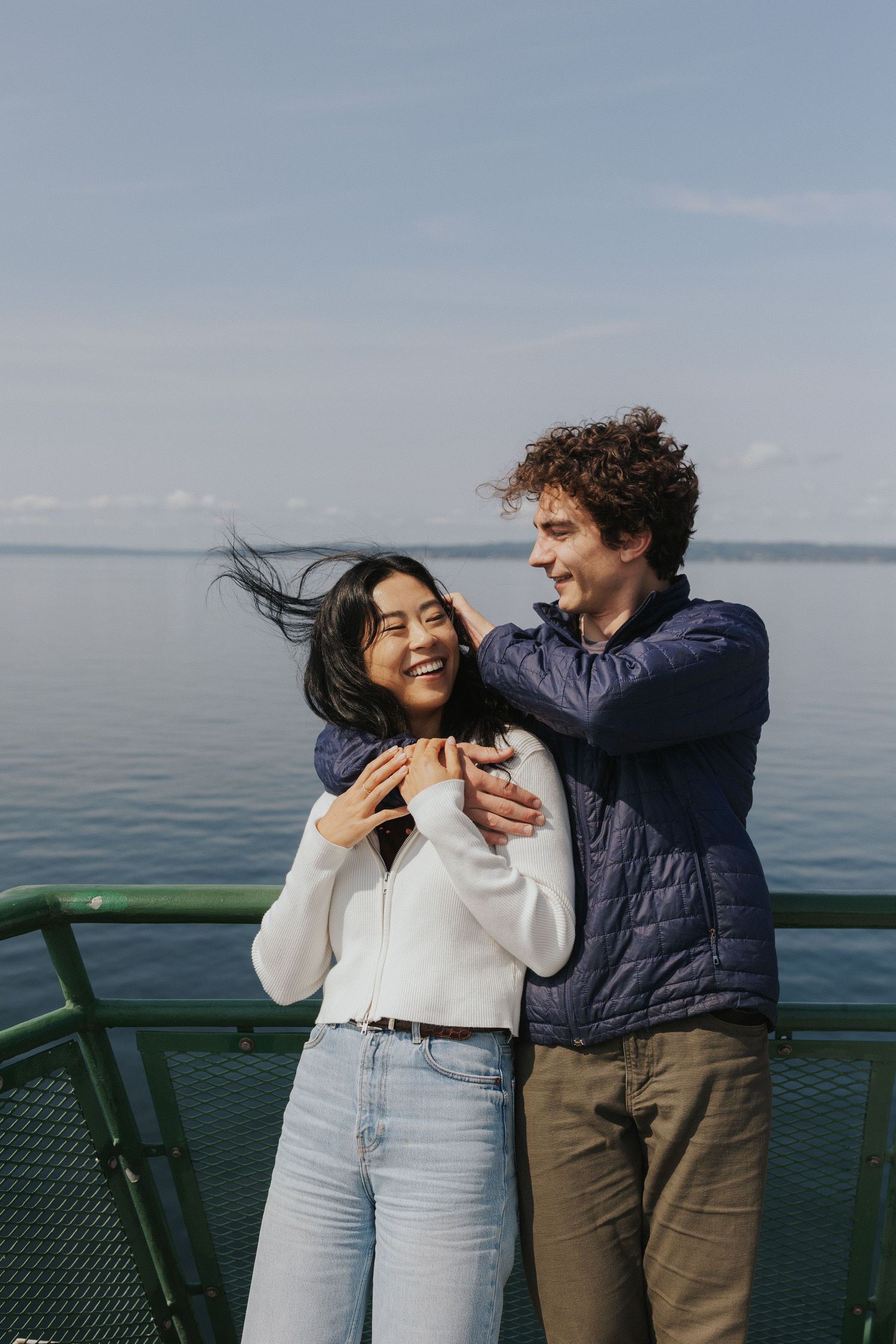 A couple shares joyful moments together on a waterfront observation deck with calm waters behind them.