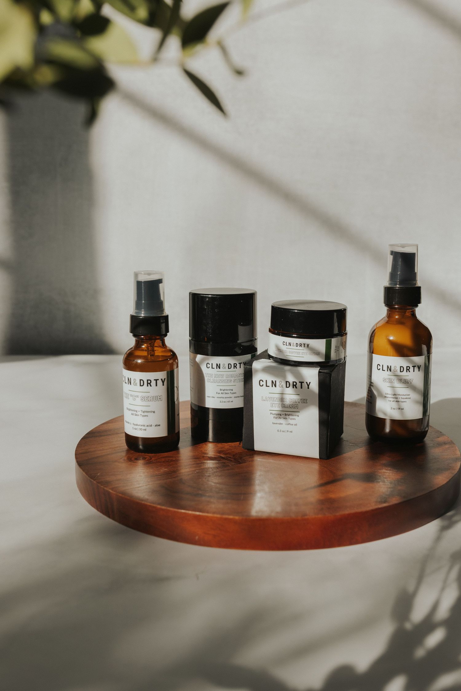 Minimalist product bottles and containers arranged on a round wooden tray with natural lighting.