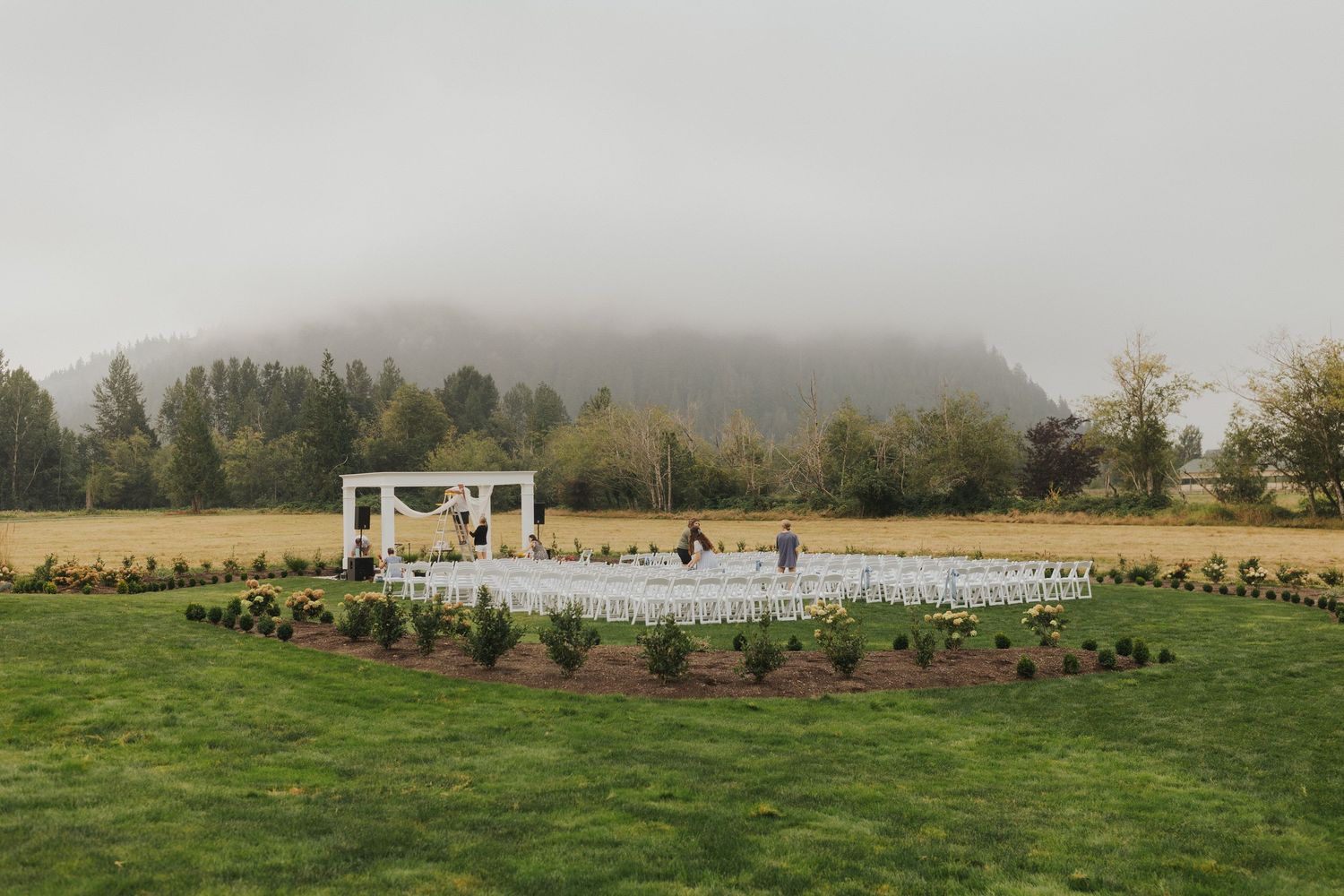 Wide landscape view of an elegant wedding venue with white chairs set up outdoors.