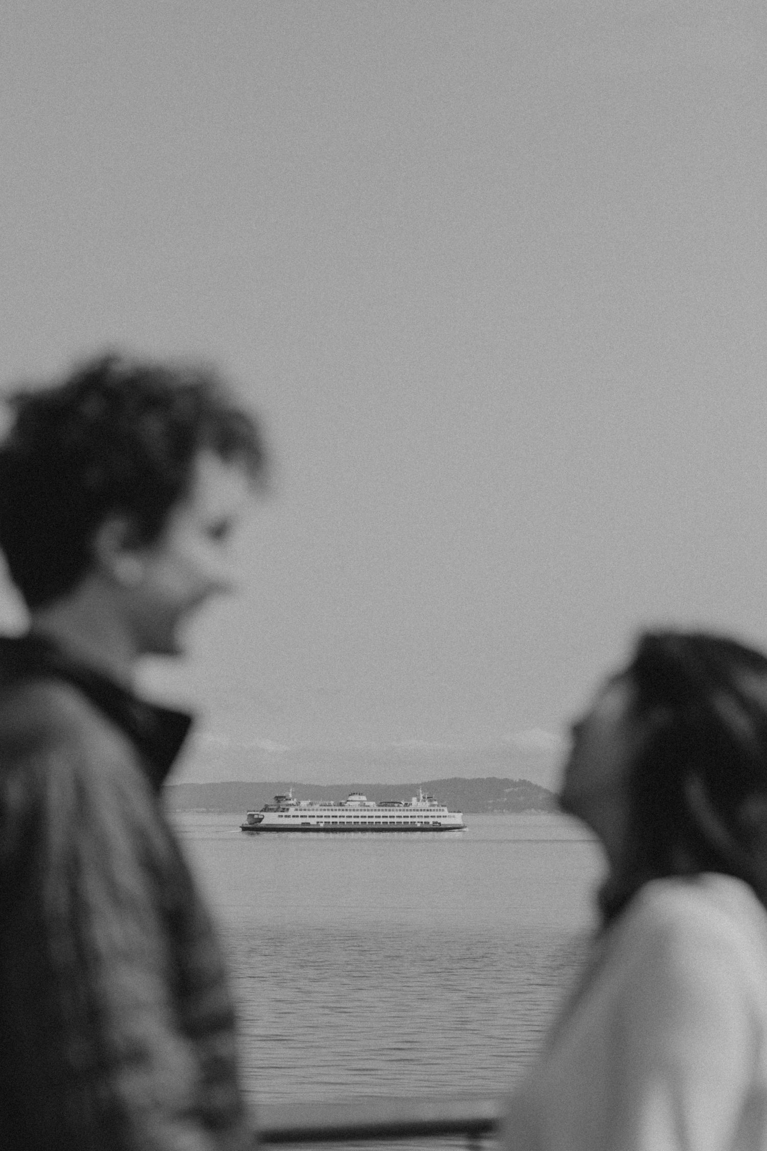 Blurred black and white scene of people on ferry deck with distant cruise ship.