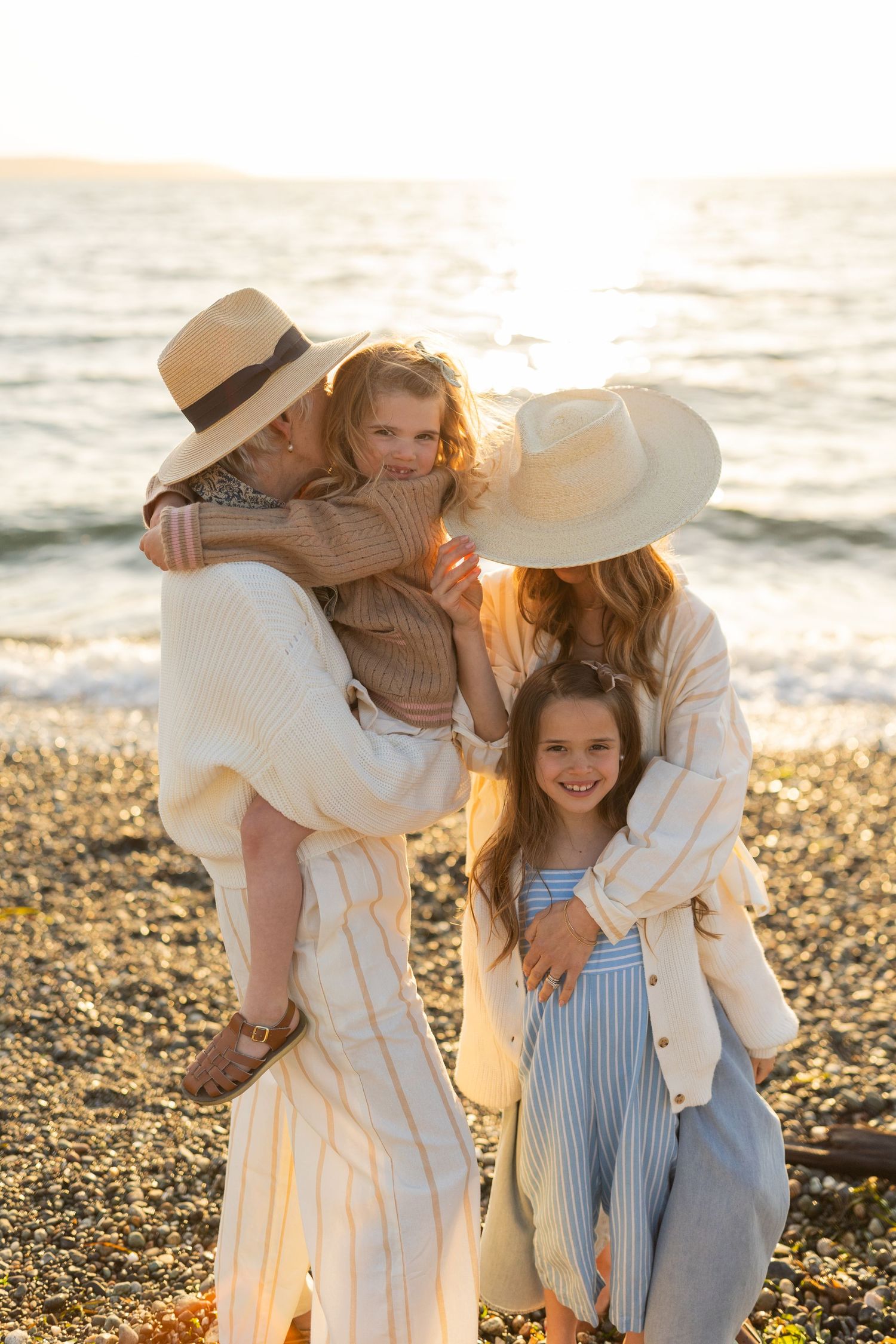 A heartwarming sunset beach photoshoot showing a family in coordinated neutral outfits on a pebble shore.