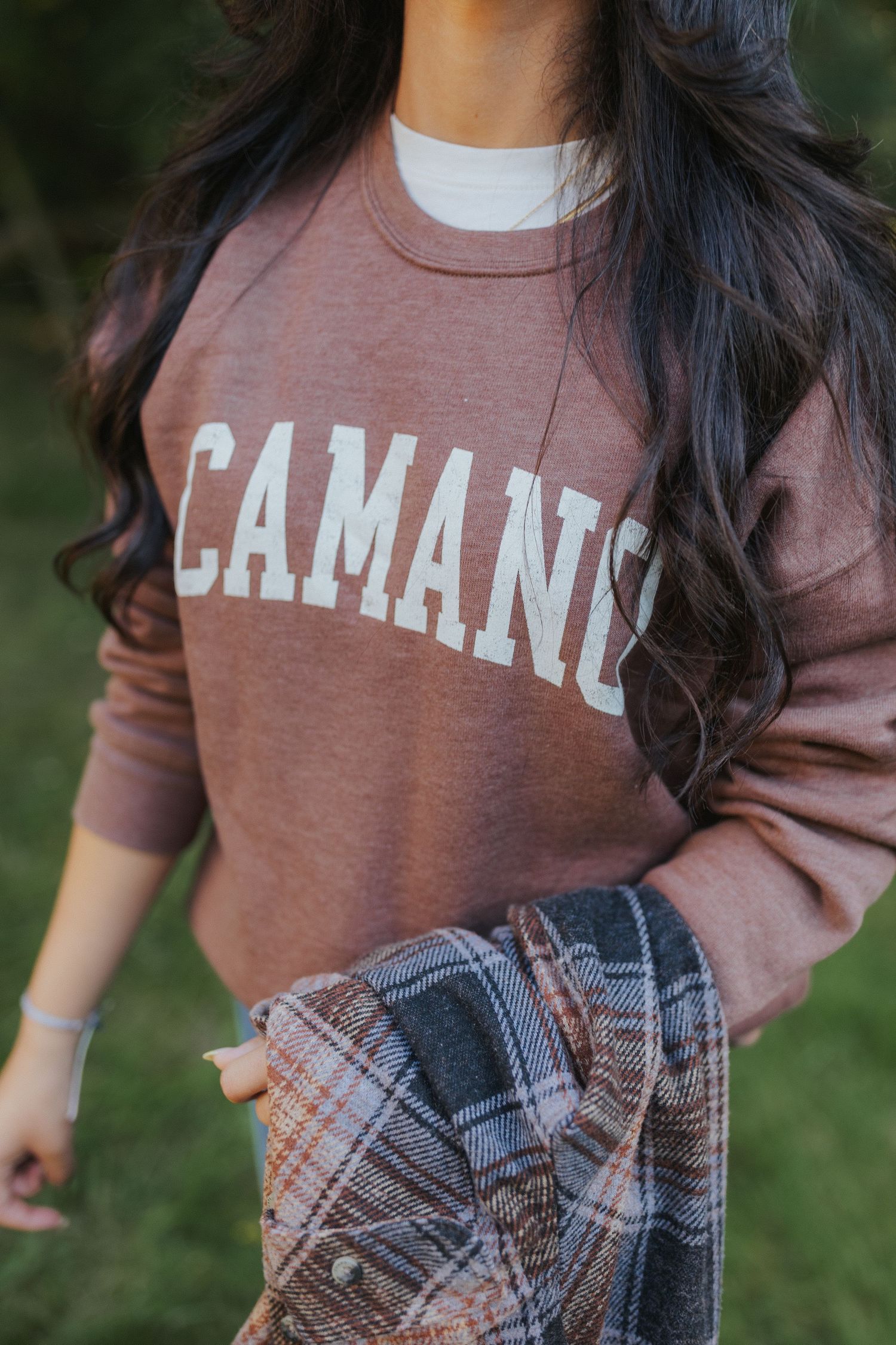Close-up of brown sweatshirt with CAMANO text and plaid flannel shirt.
