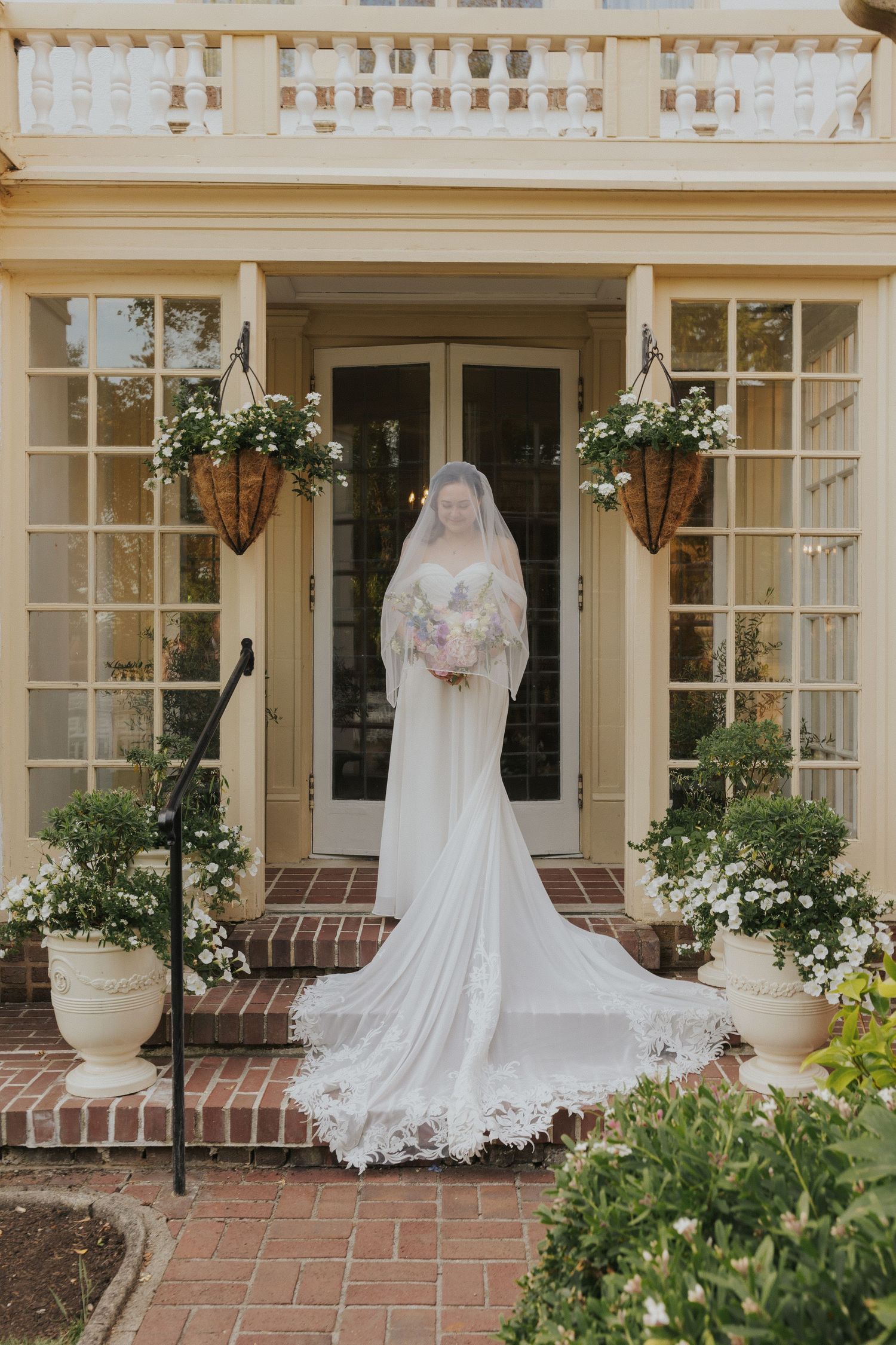 Wedding dress with flowing train photographed outside colonial style venue entrance.