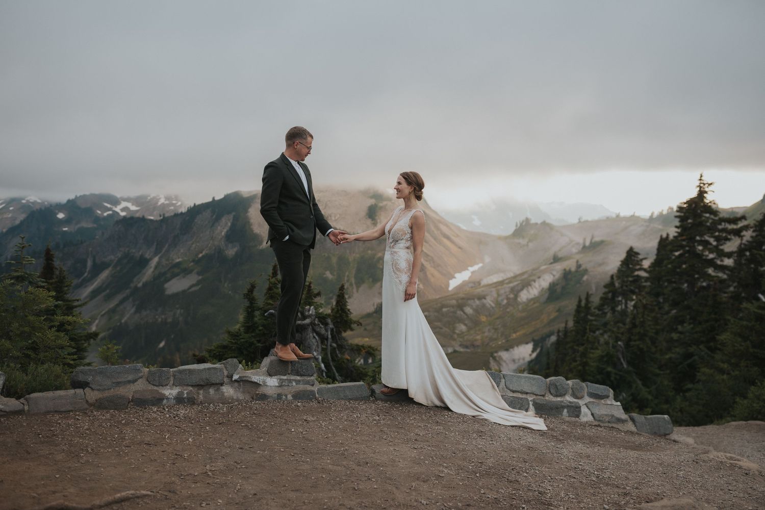 Wedding couple stands together on mountain ridge with expansive valley views.