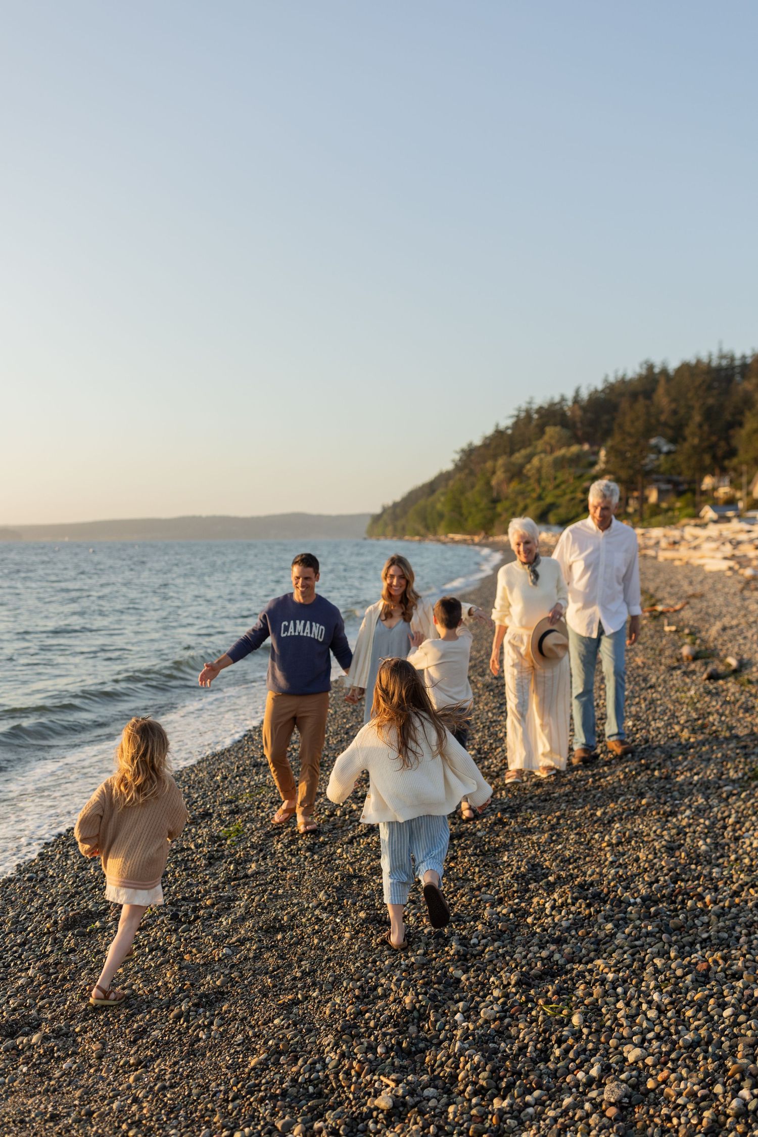 Group walking together on a scenic rocky beach with evergreen trees in the background.