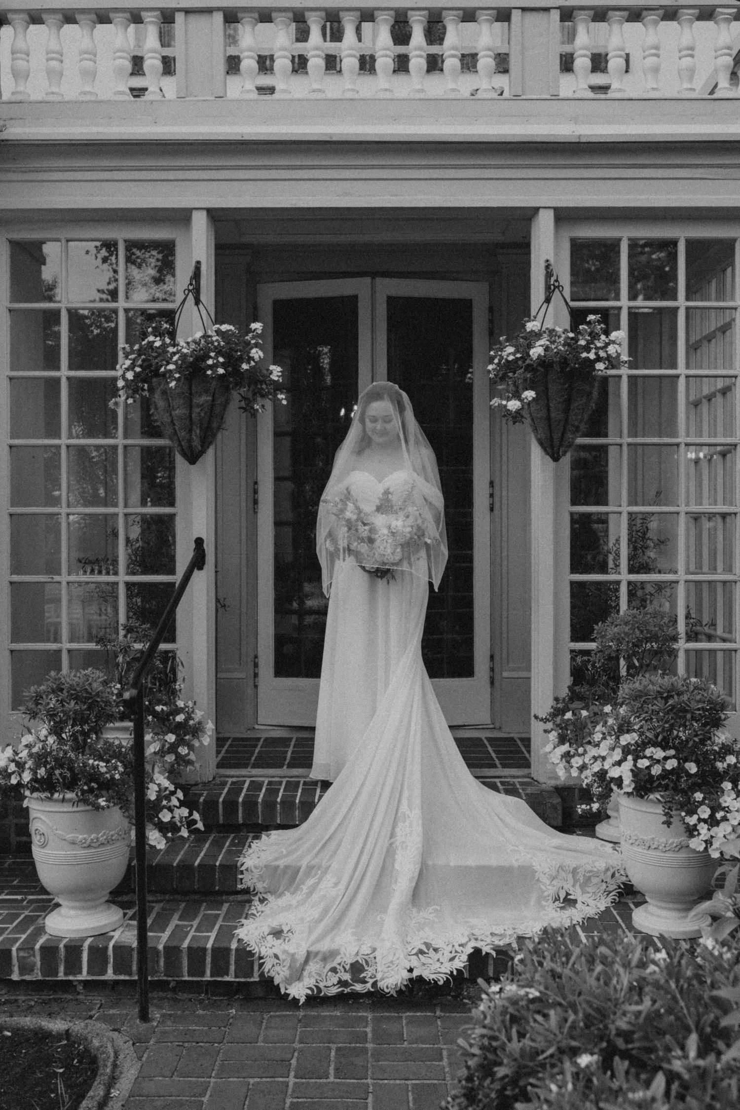 Black and white photo of wedding gowns displayed on a classic colonial porch with brick details.