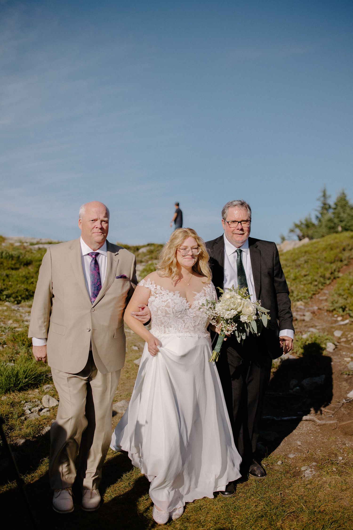 Wedding group walks together along a scenic mountain path during an outdoor ceremony.