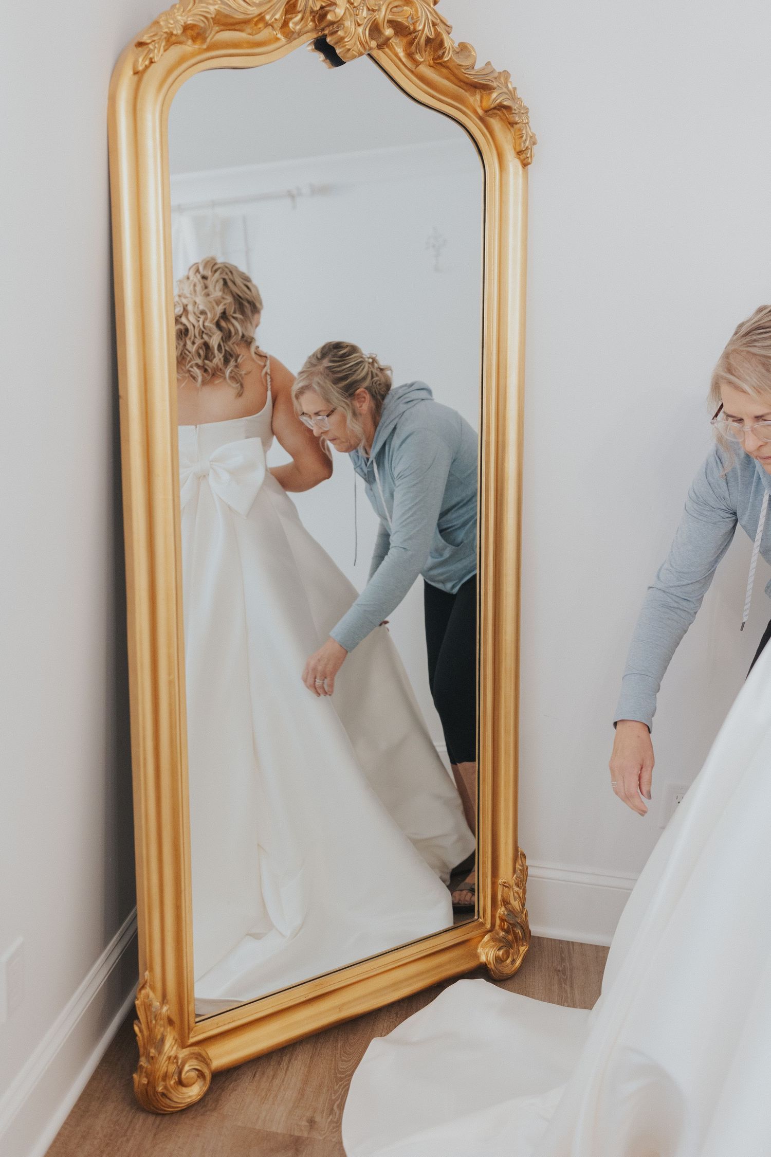 Ornate gold-framed mirror being positioned against a white wall.
