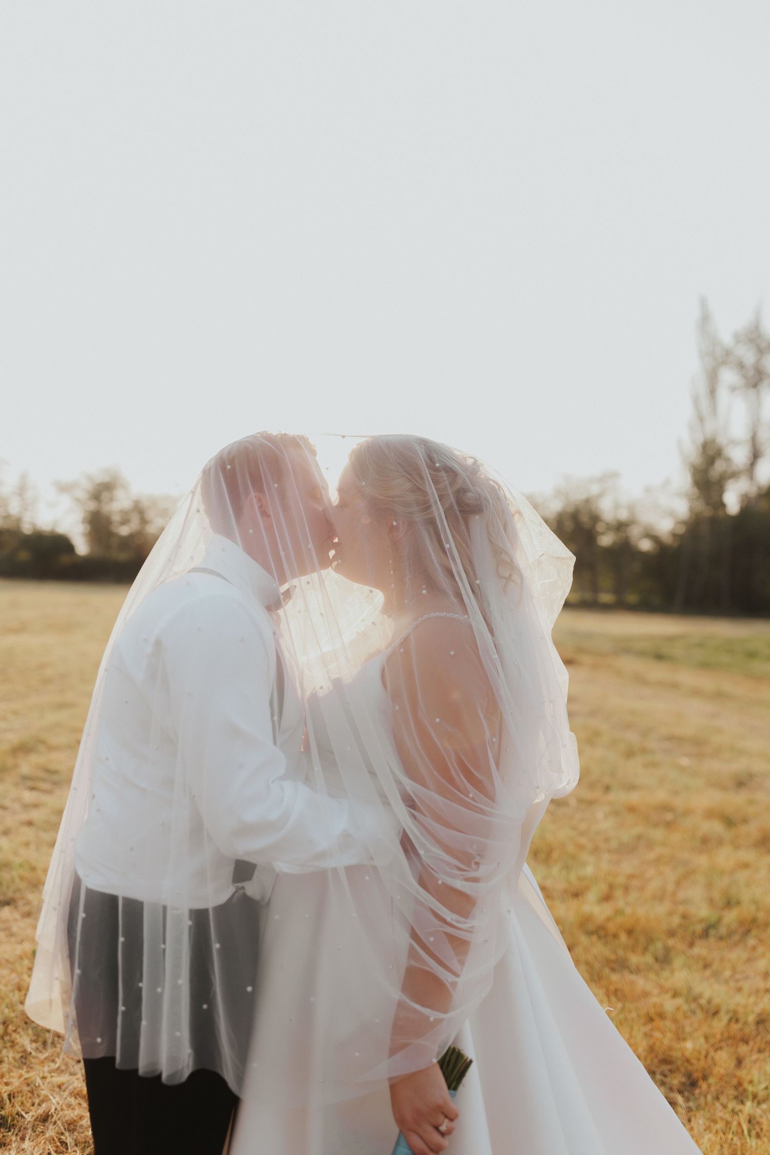 Soft focus wedding photo with white veil and dress details in golden sunlight.