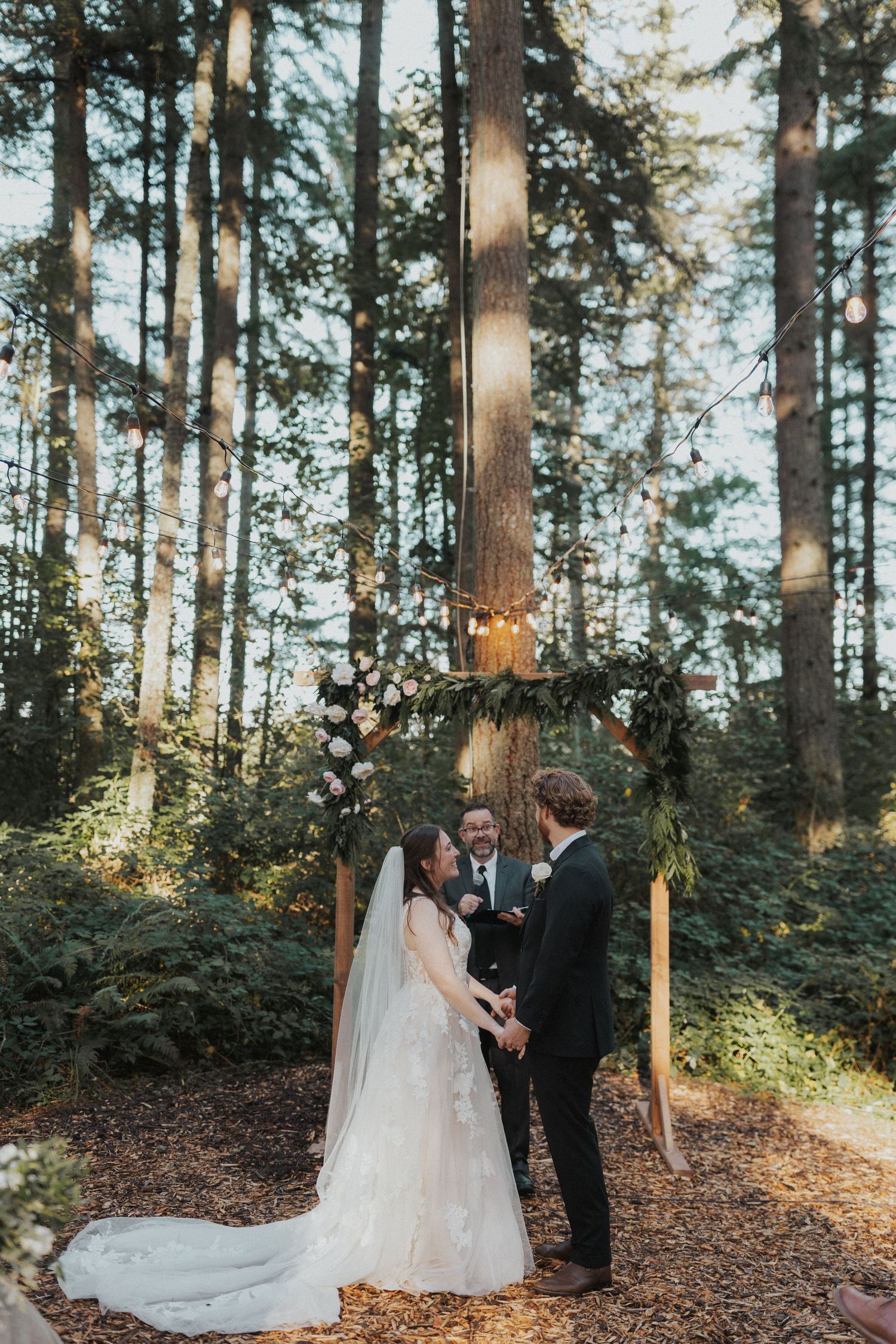 A romantic forest wedding ceremony beneath tall pine trees at golden hour.
