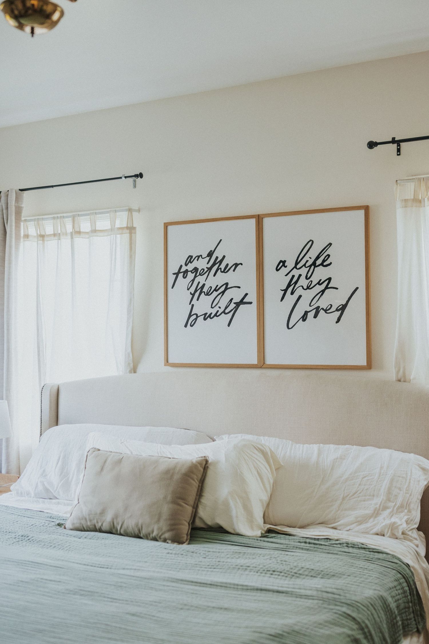 Minimalist bedroom with framed calligraphy art above white bedding and sage green accents.