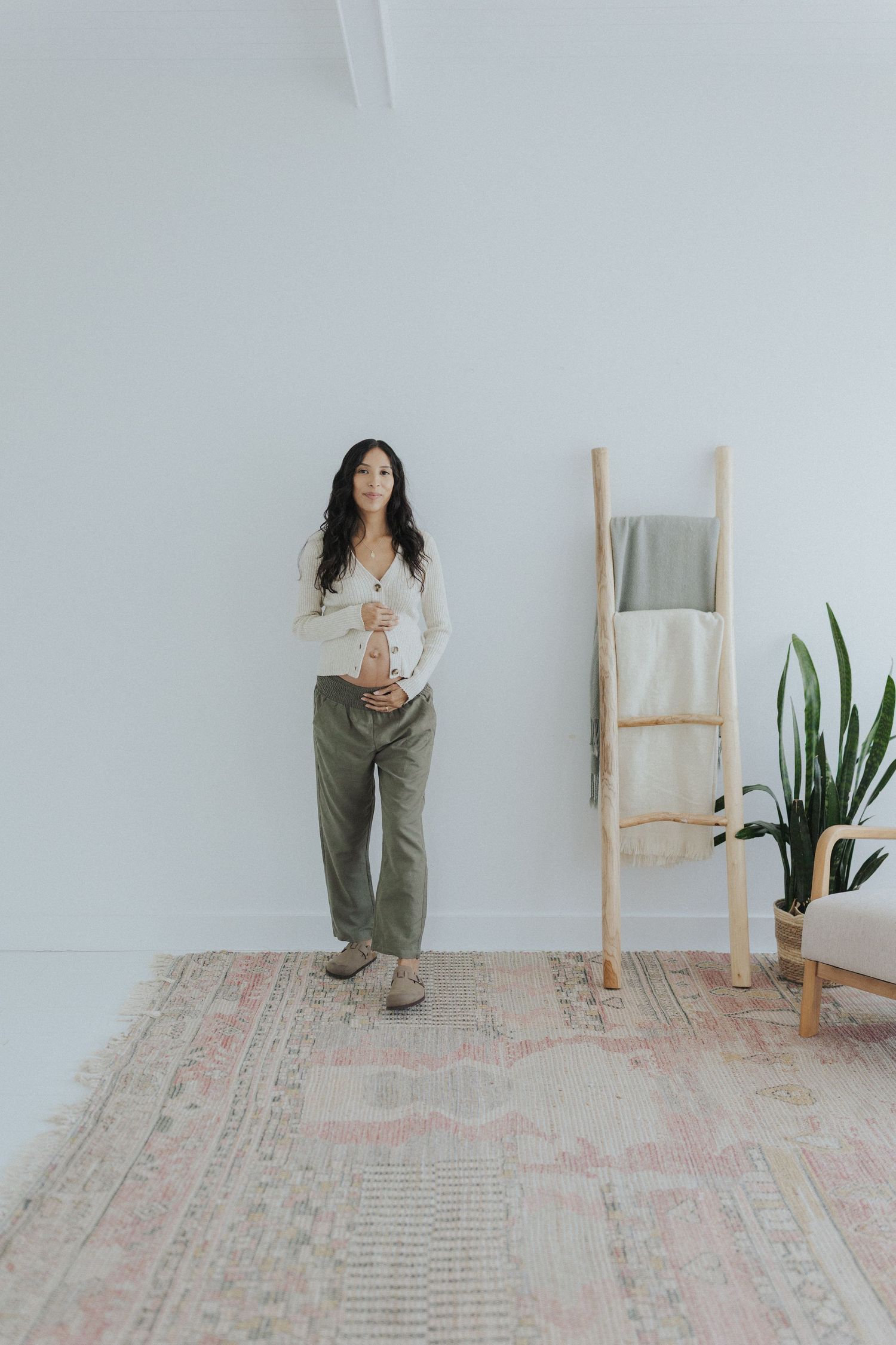 Minimalist white room with wooden ladder, plants, and patterned rug.
