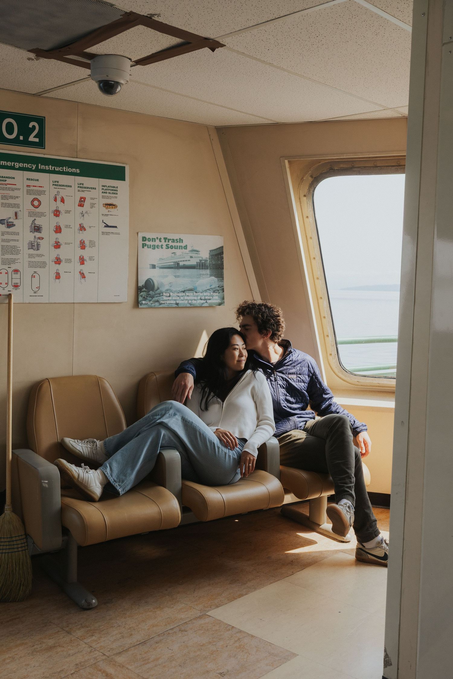 Interior of ferry cabin with passengers resting on brown leather benches.