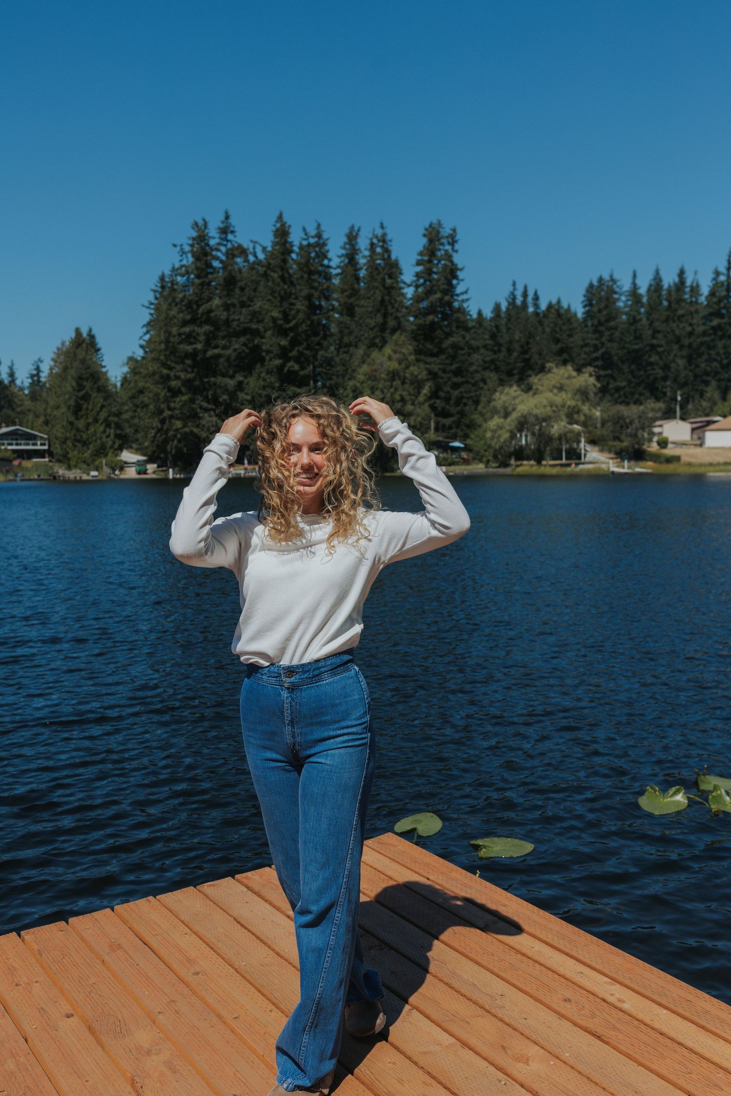 Someone dances joyfully on a wooden dock with a scenic lake and pine trees in the background.