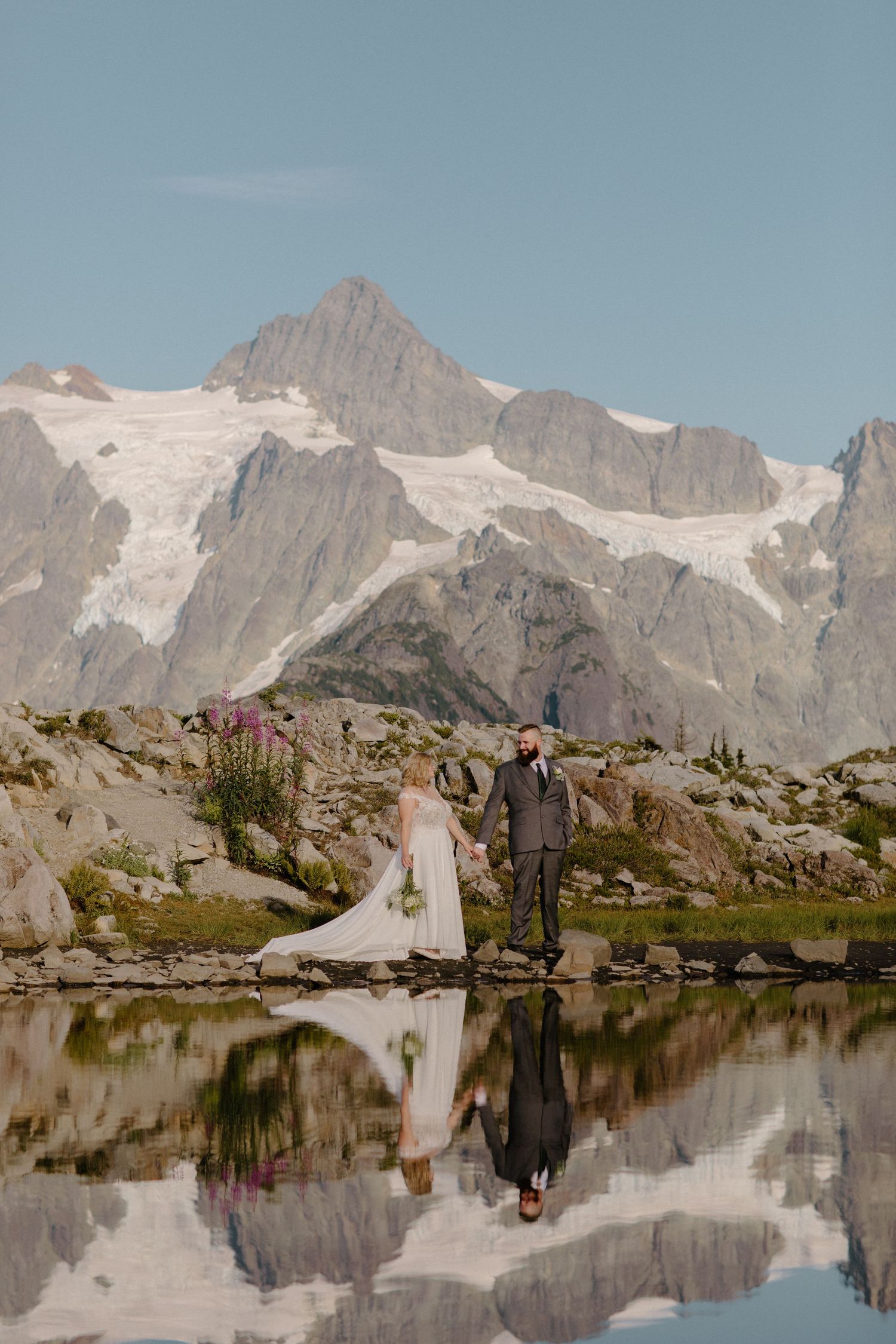 Snow-capped mountain peaks reflect perfectly in alpine lake during wedding photography.