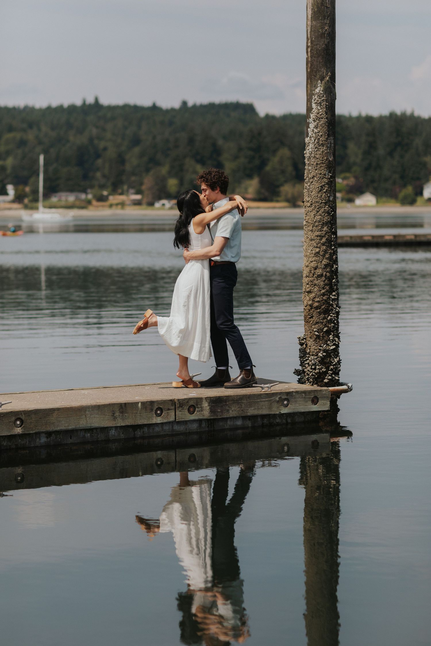 Two people dancing on wooden dock over reflective water with forest backdrop.