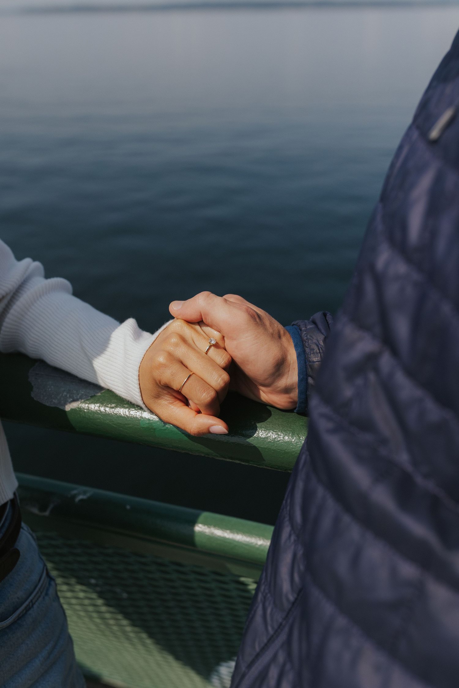 Close-up of hands resting on a green railing against a blurred ocean backdrop.