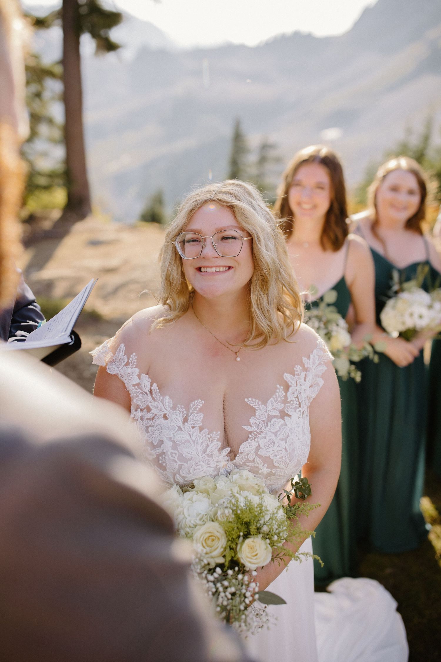 A white wedding dress with delicate lace details is worn during an outdoor mountain ceremony.