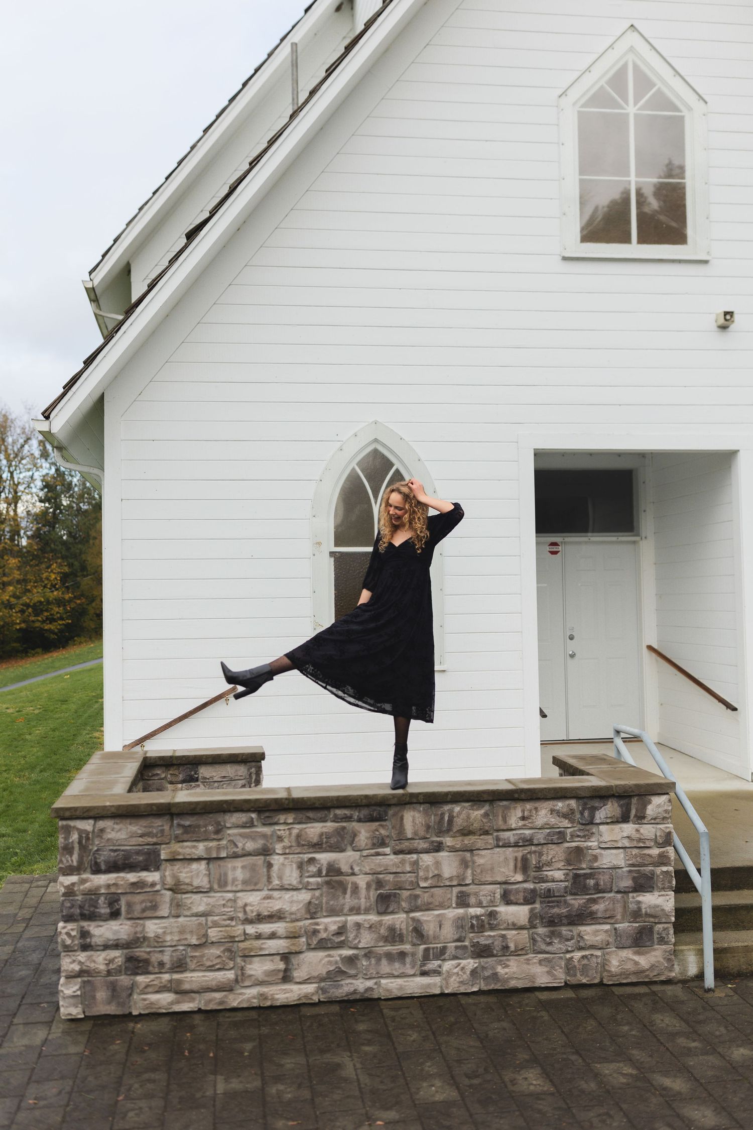 A series of photos showing someone in black clothing posing near a white church building with stone foundation.