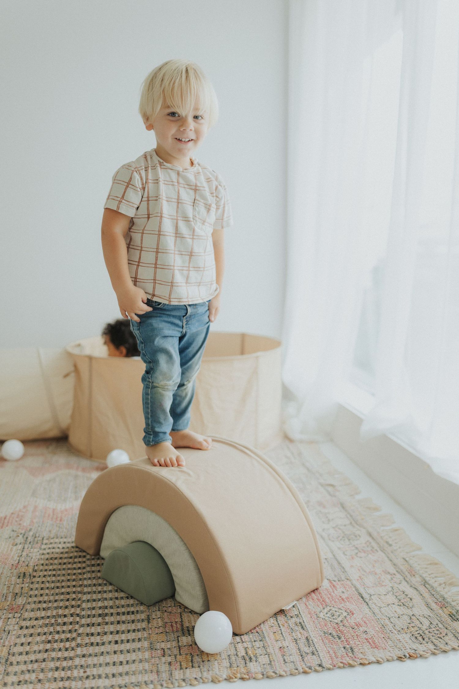 Child standing on DIY cardboard car toy against white wall.