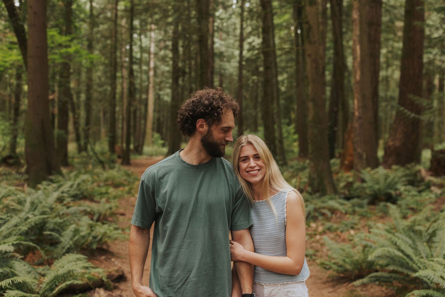 Couple sharing intimate moments on a forest path surrounded by evergreen trees.