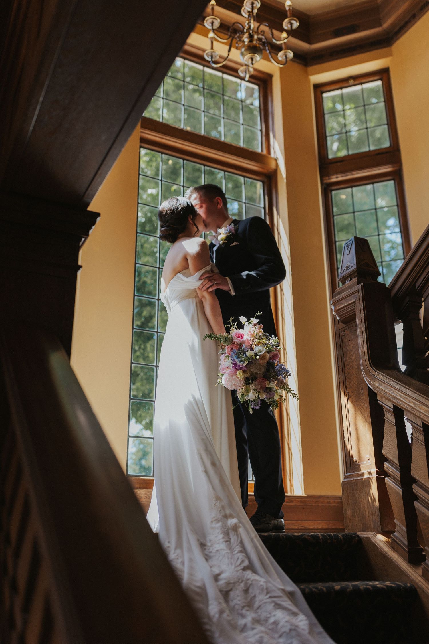 Romantic staircase portrait of a couple in wedding attire with natural window lighting.