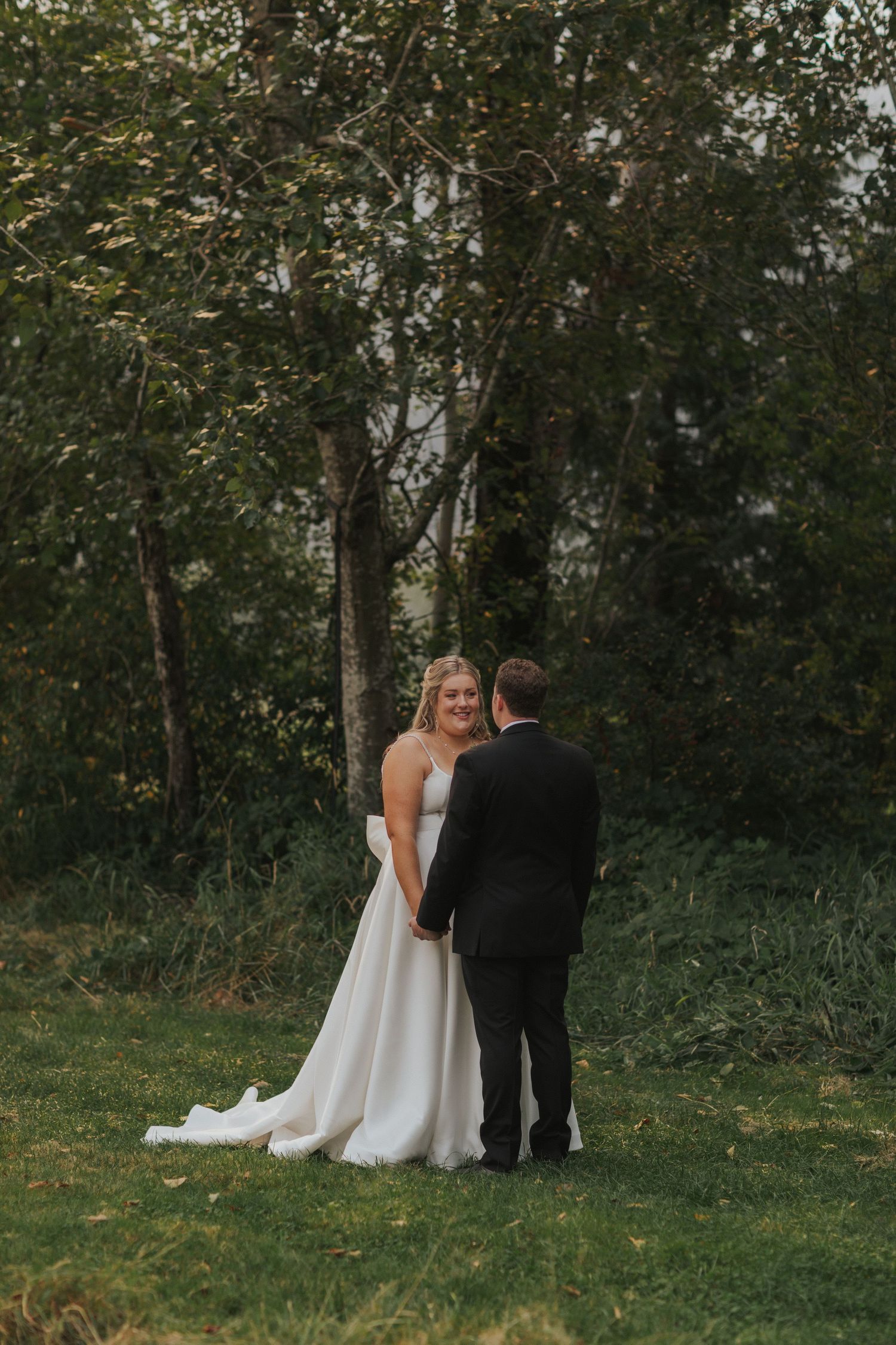 A wedding couple shares an intimate moment on a grassy hill with a wooded backdrop.