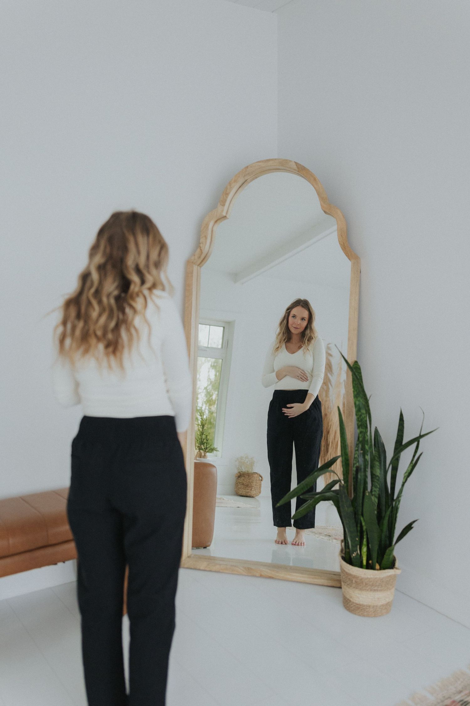 Person moving dynamically in front of arched mirror in white minimalist room.
