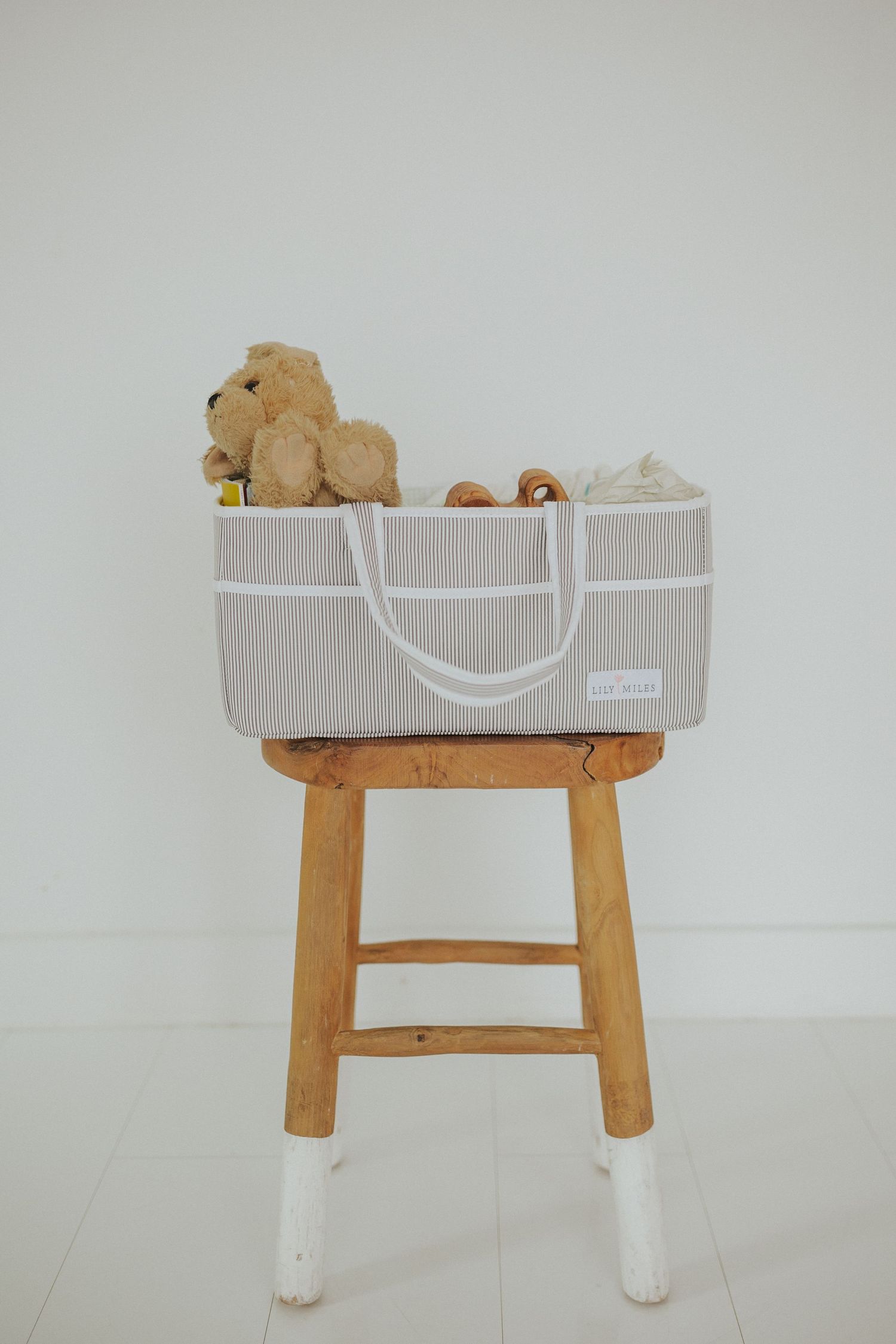 A gray storage basket with wooden legs containing stuffed animals and toys.