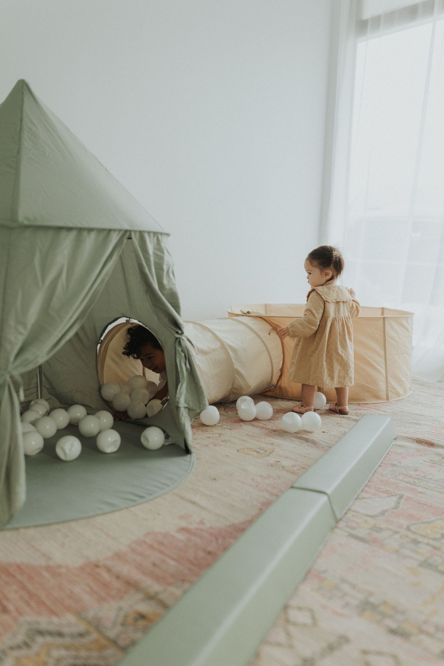 Green tent setup indoors with play tunnel on pink patterned rug.