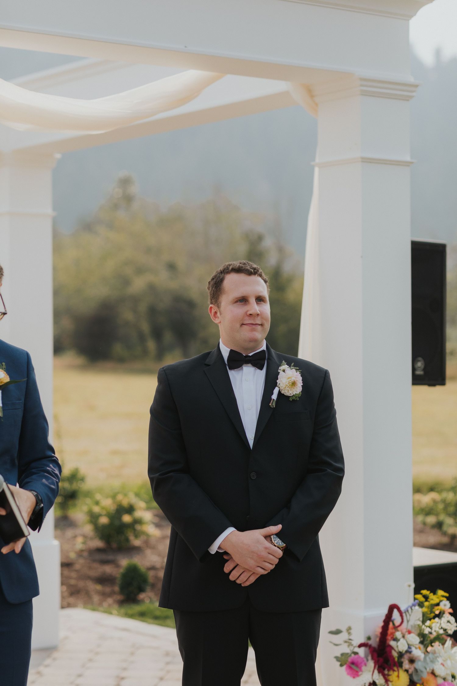 Wedding ceremony setup with white columns and elegant decor against a pastoral landscape.