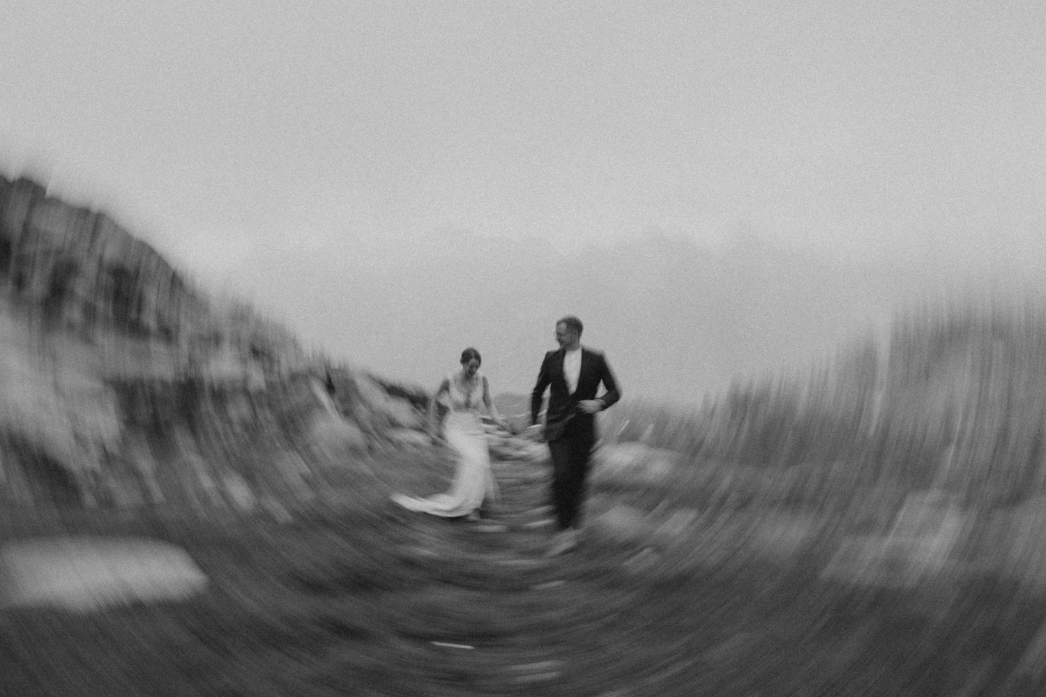 Artistic blurred black and white panorama of wedding couple on mountain ridge.