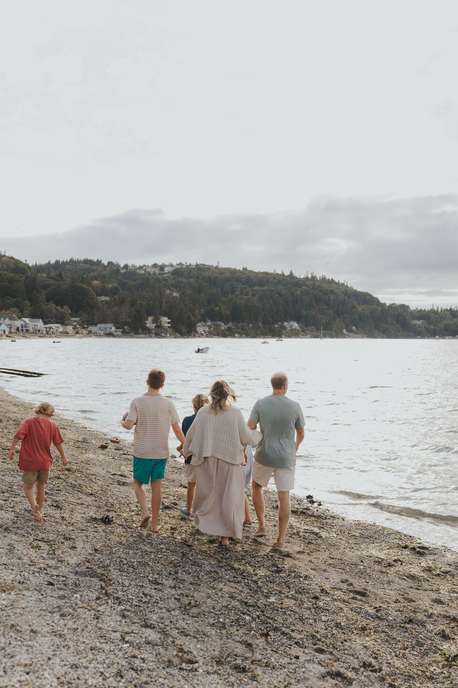 Group walking along a scenic rocky beach with mountains in the background on an overcast day.