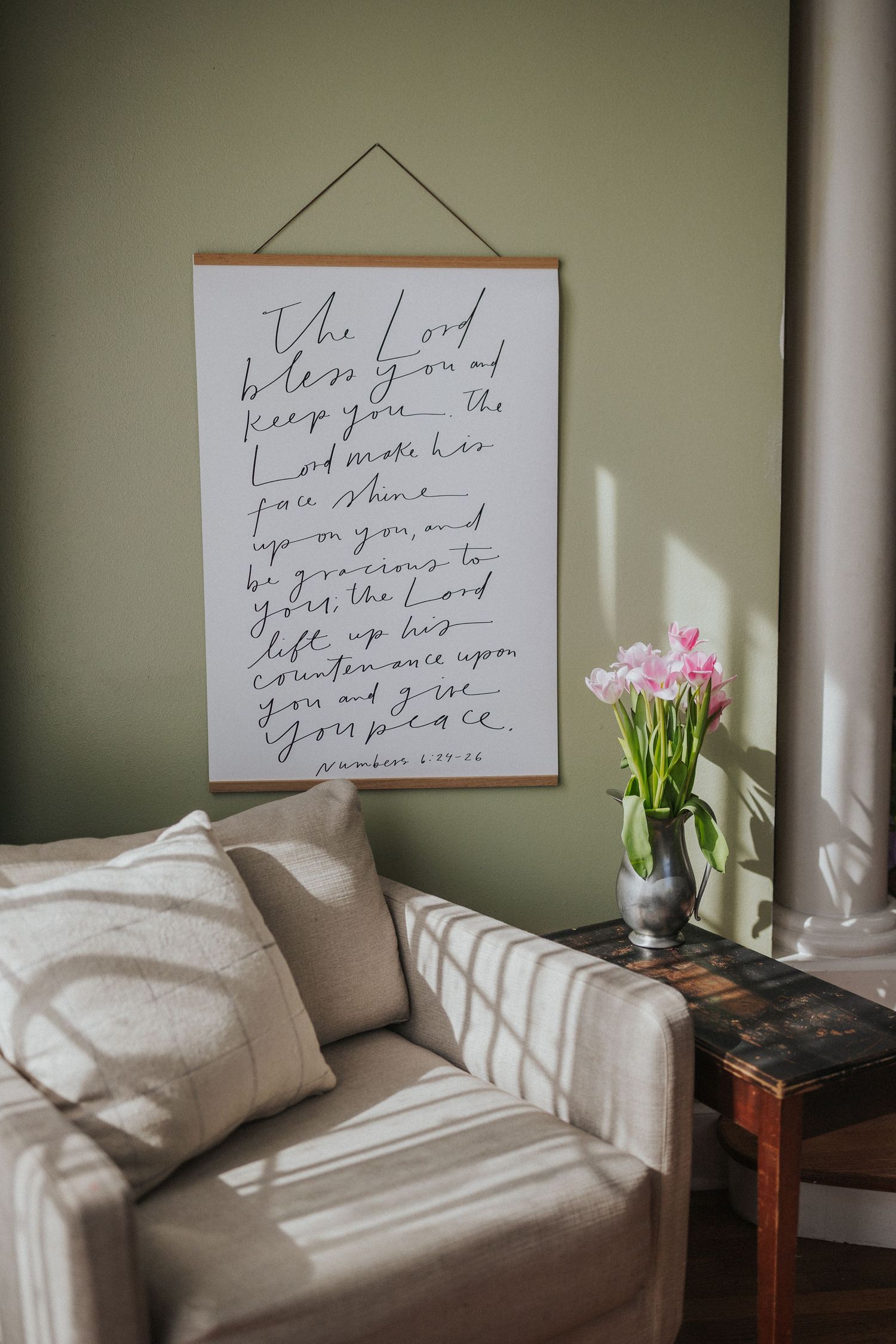 Cozy bedroom corner with handwritten art, white pillows, and fresh flowers on side table.