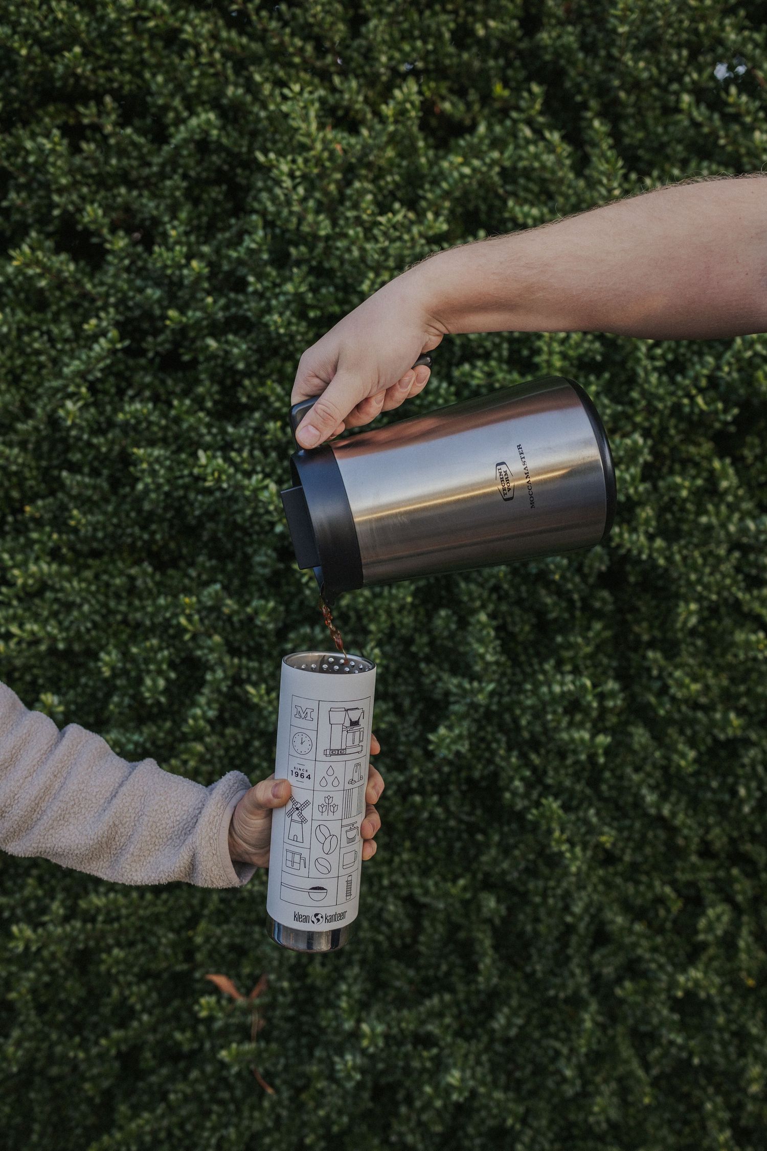 Demonstration of pouring coffee from stainless steel thermos into patterned ceramic mug.