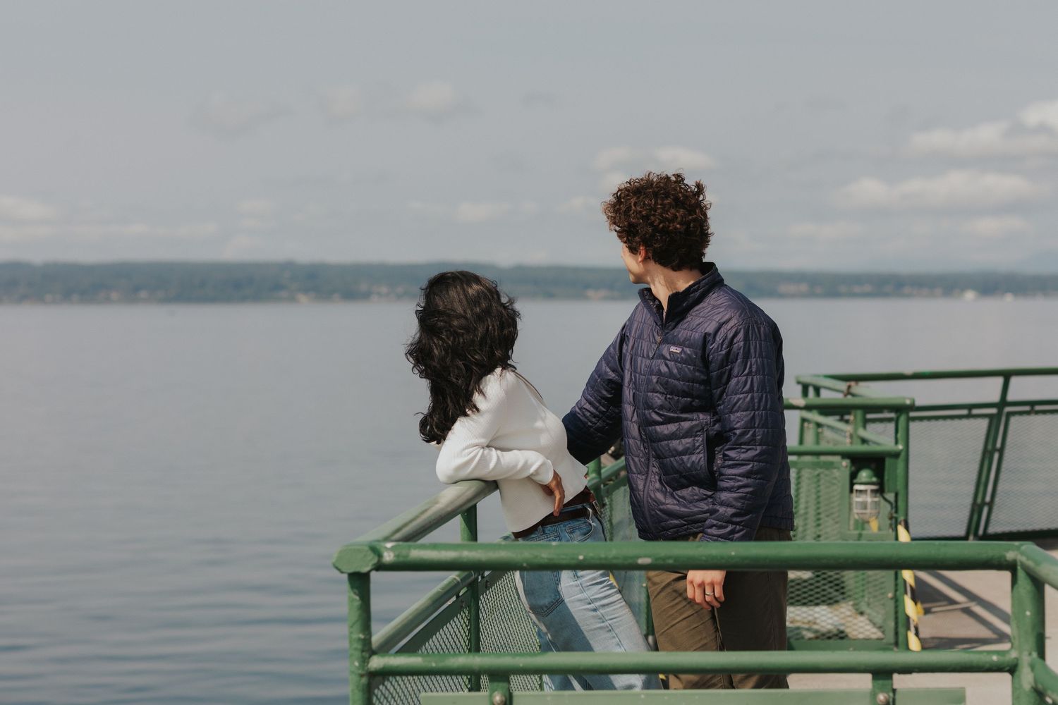 Two people share a romantic moment on an oceanfront viewing platform under clear skies.