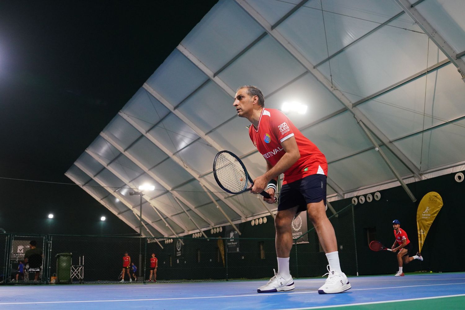 Tennis player practicing serves in an indoor sports facility with white dome ceiling.