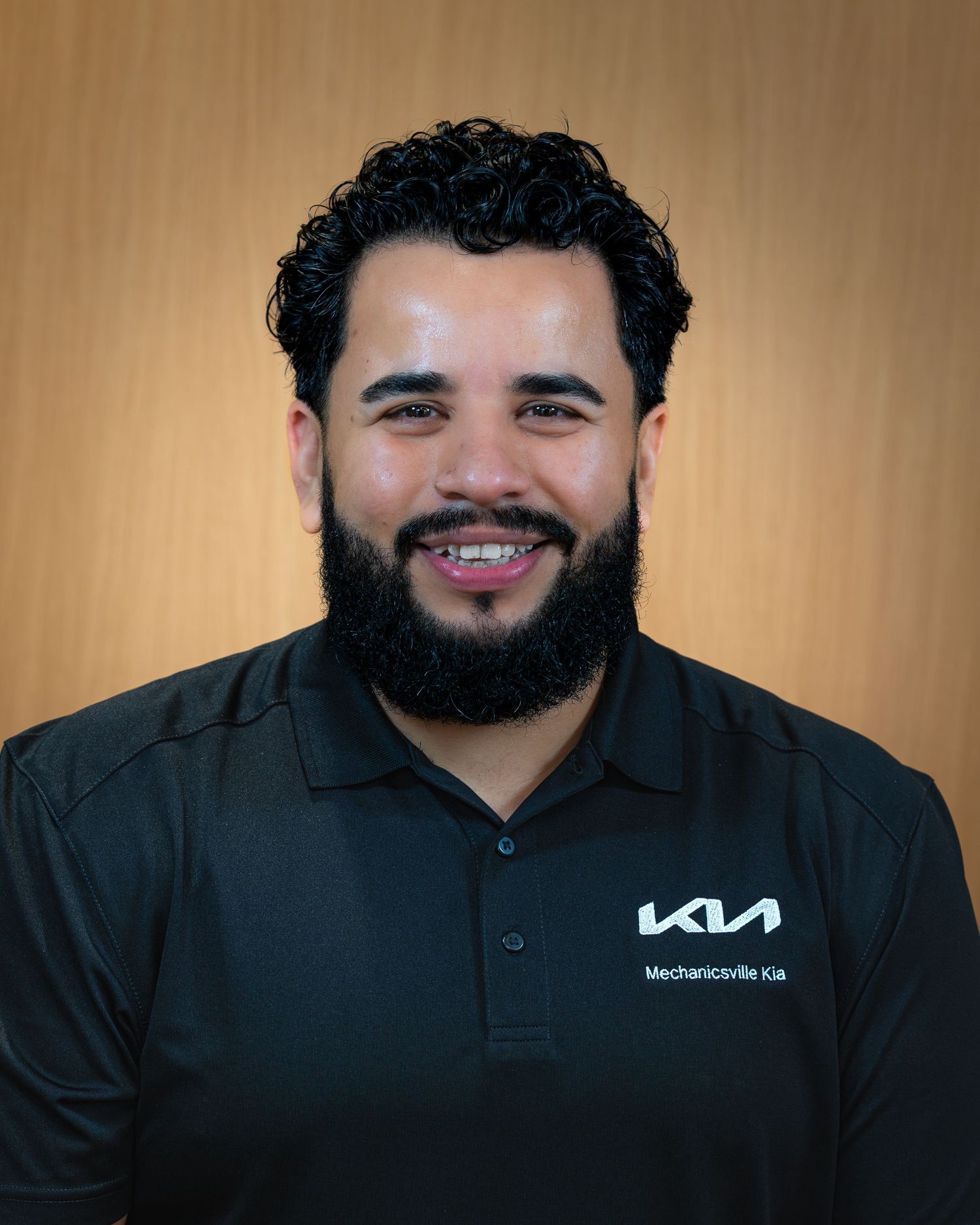 Person wearing a black polo shirt smiles at the camera in a professional headshot series.